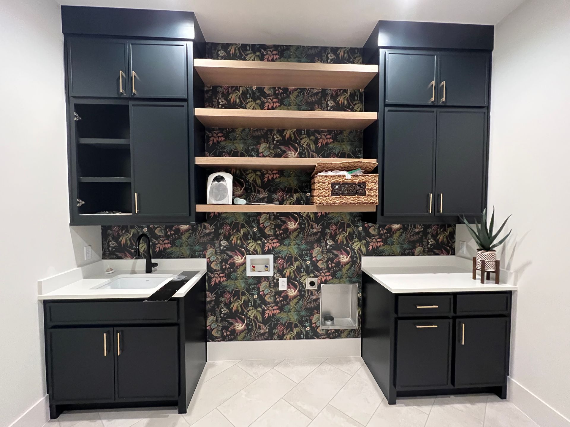Laundry room with dark blue cabinets, white countertops, floral wallpaper, and wood shelves.