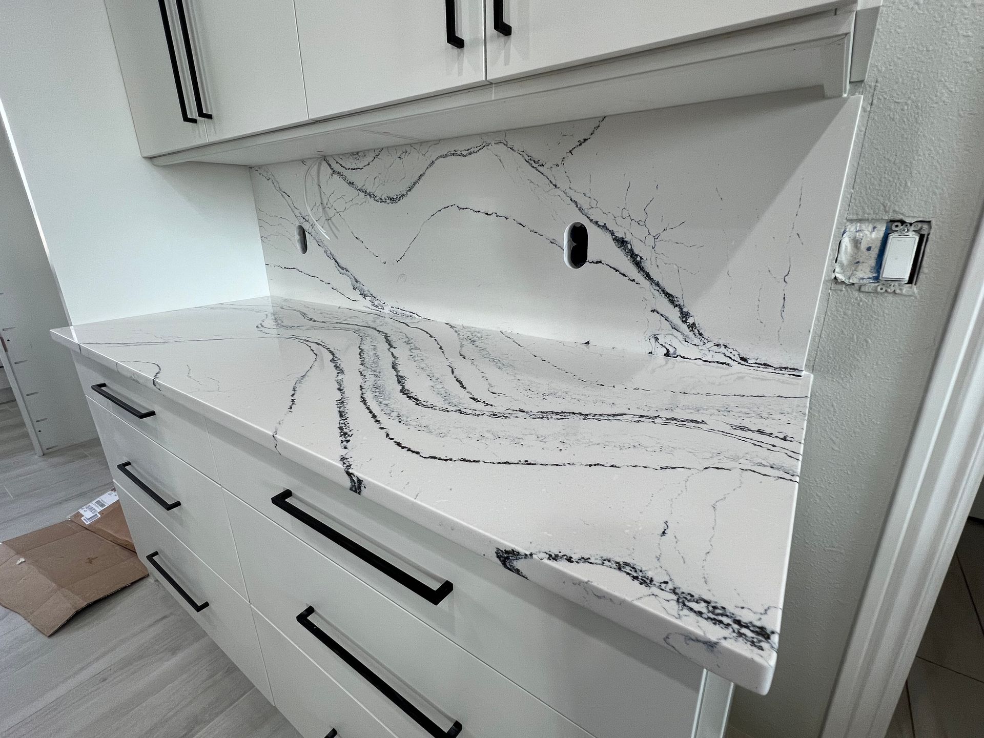 White kitchen countertop with black veining, matching backsplash, and white cabinets with black handles.