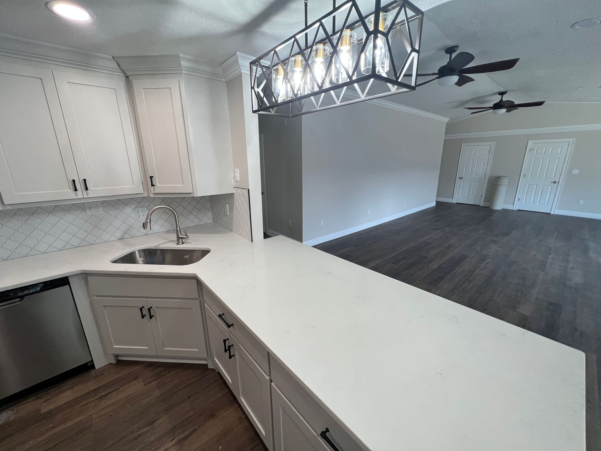 Modern kitchen with white cabinets, stainless steel appliances, and a long countertop. Dark wood floors.