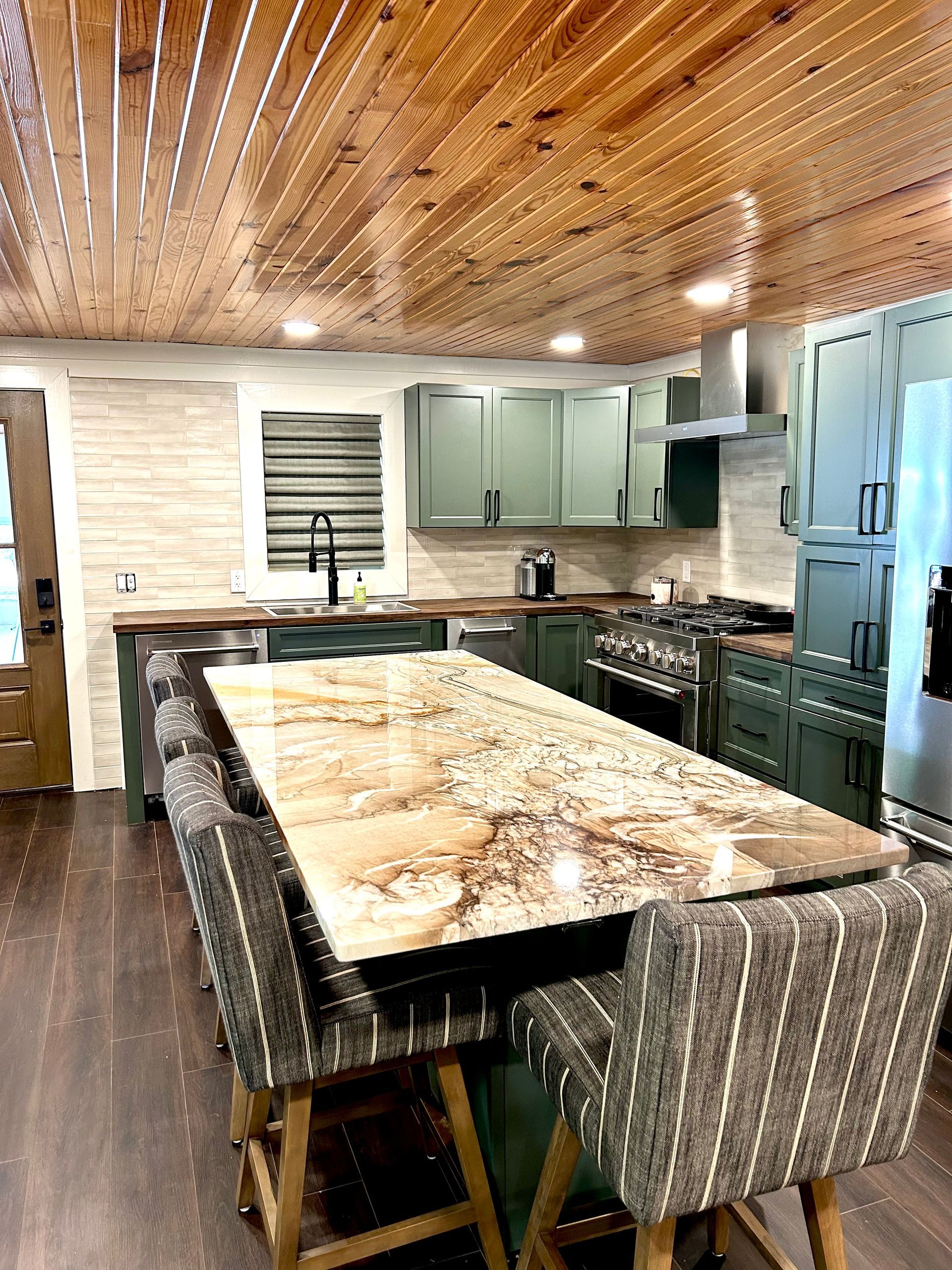 Green kitchen with granite island and wood ceiling. Bar stools and appliances.