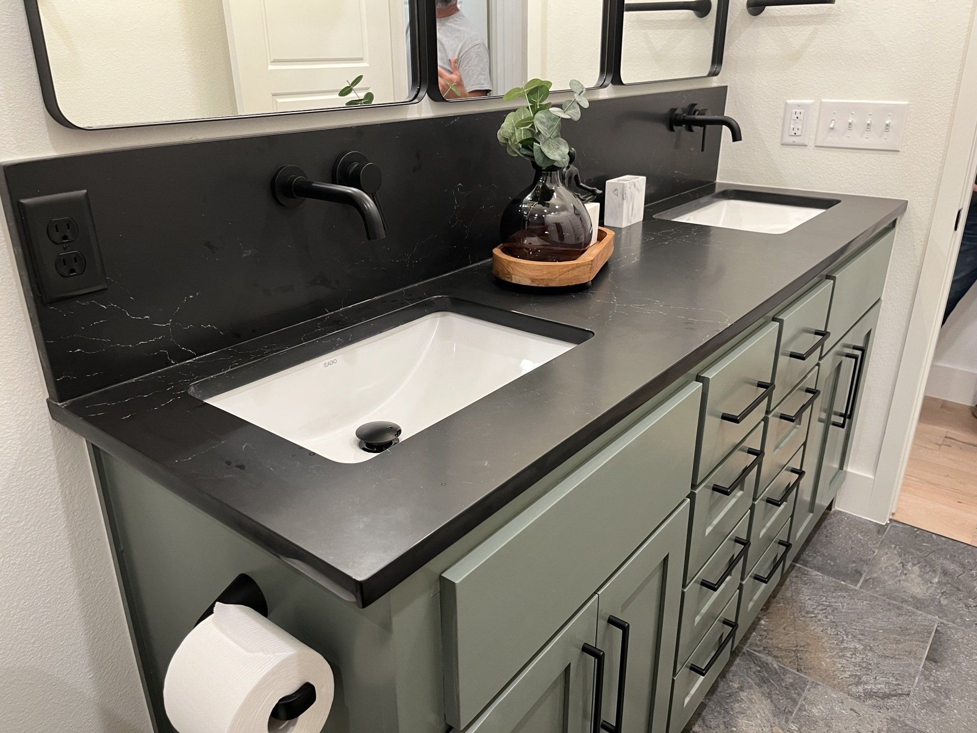 Green bathroom vanity with black countertop, sinks, and faucets.