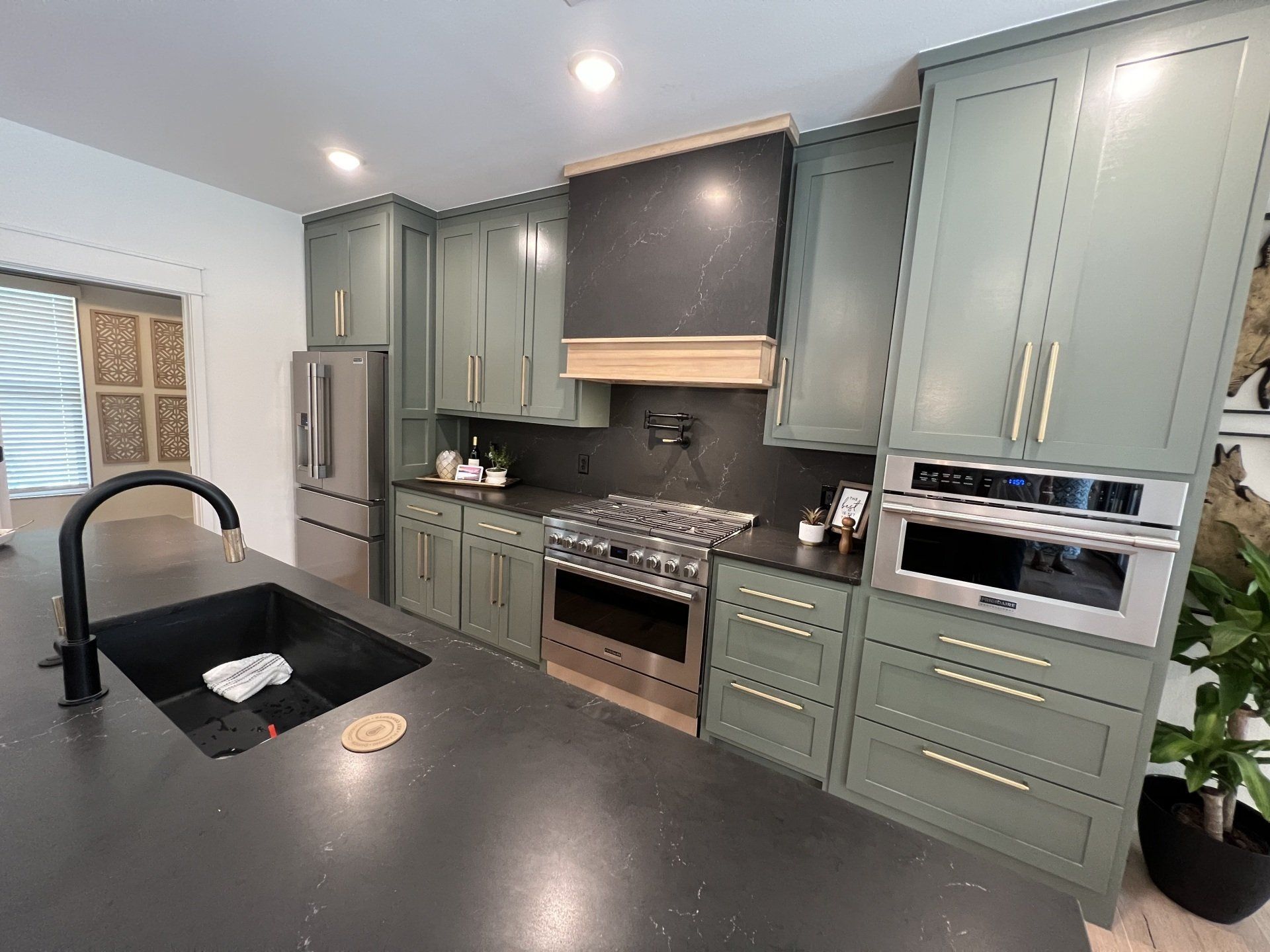 Green kitchen cabinets with stainless steel appliances and black countertops.