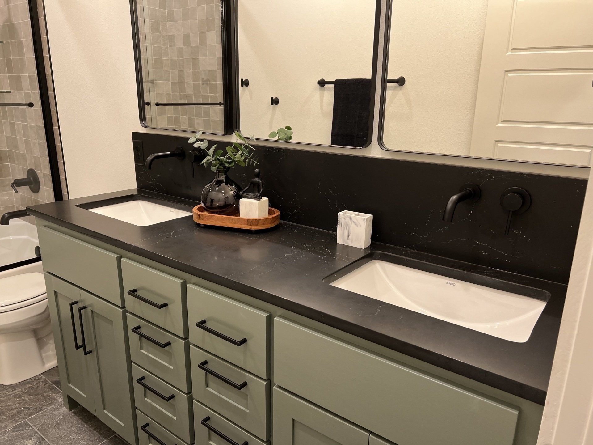 Bathroom with green vanity, dark countertop, and black fixtures.