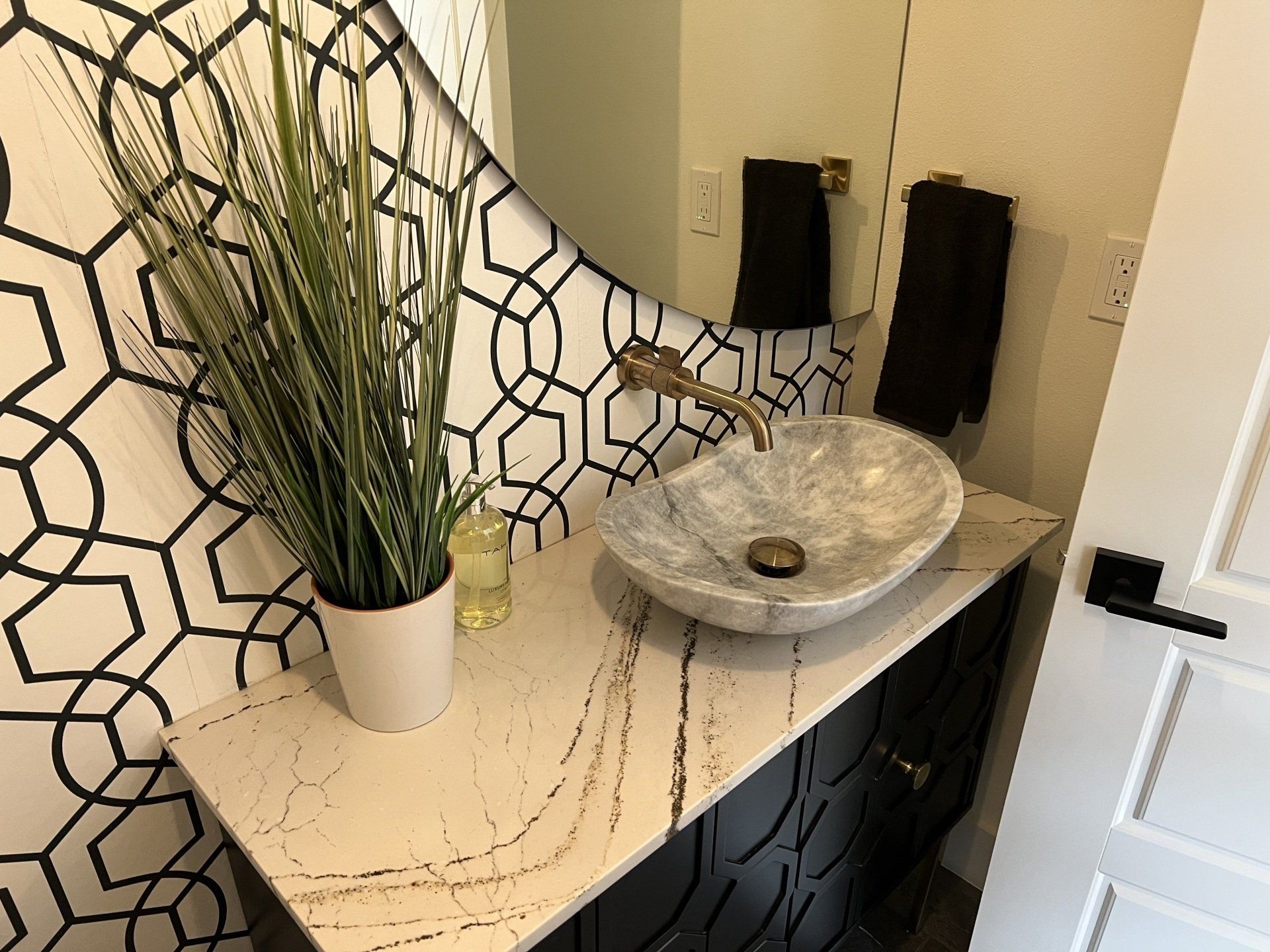 Small bathroom with patterned wallpaper, marble sink, and gold faucet.