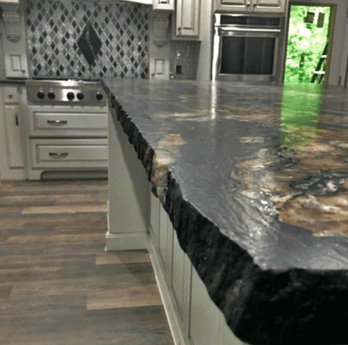 Kitchen island with rough-edged black countertop and stone backsplash, white cabinets, and stainless steel appliances.