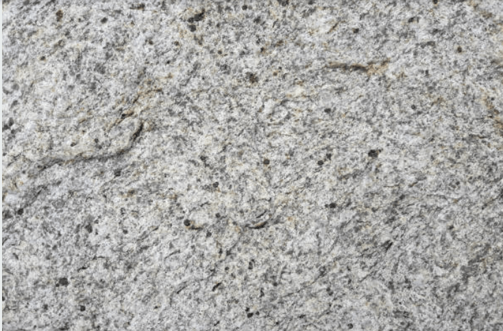 Close-up view of a rough, gray-white granite rock surface with small dark holes.