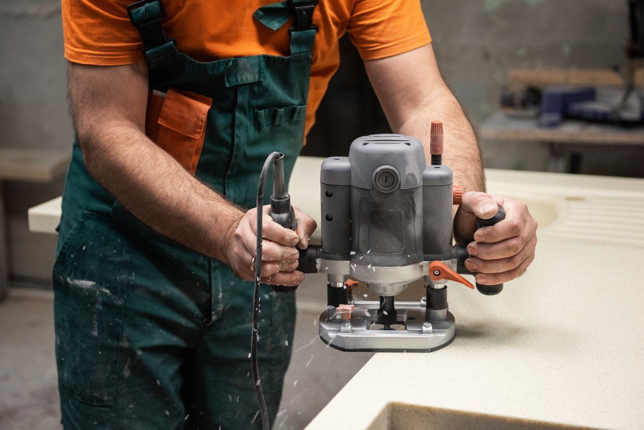 Person in overalls using a router on a wooden surface.