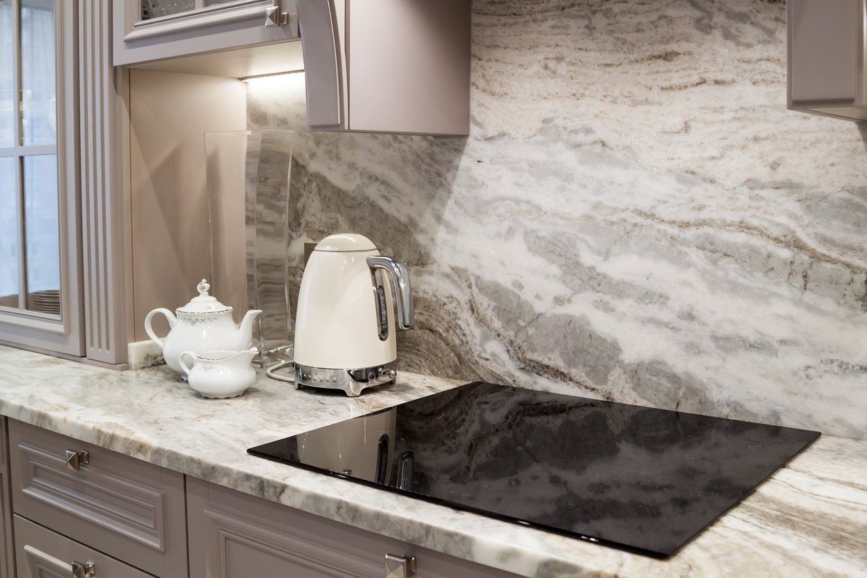 Kitchen counter with electric stove, tea kettle, and teapot. Granite backsplash and cabinets.