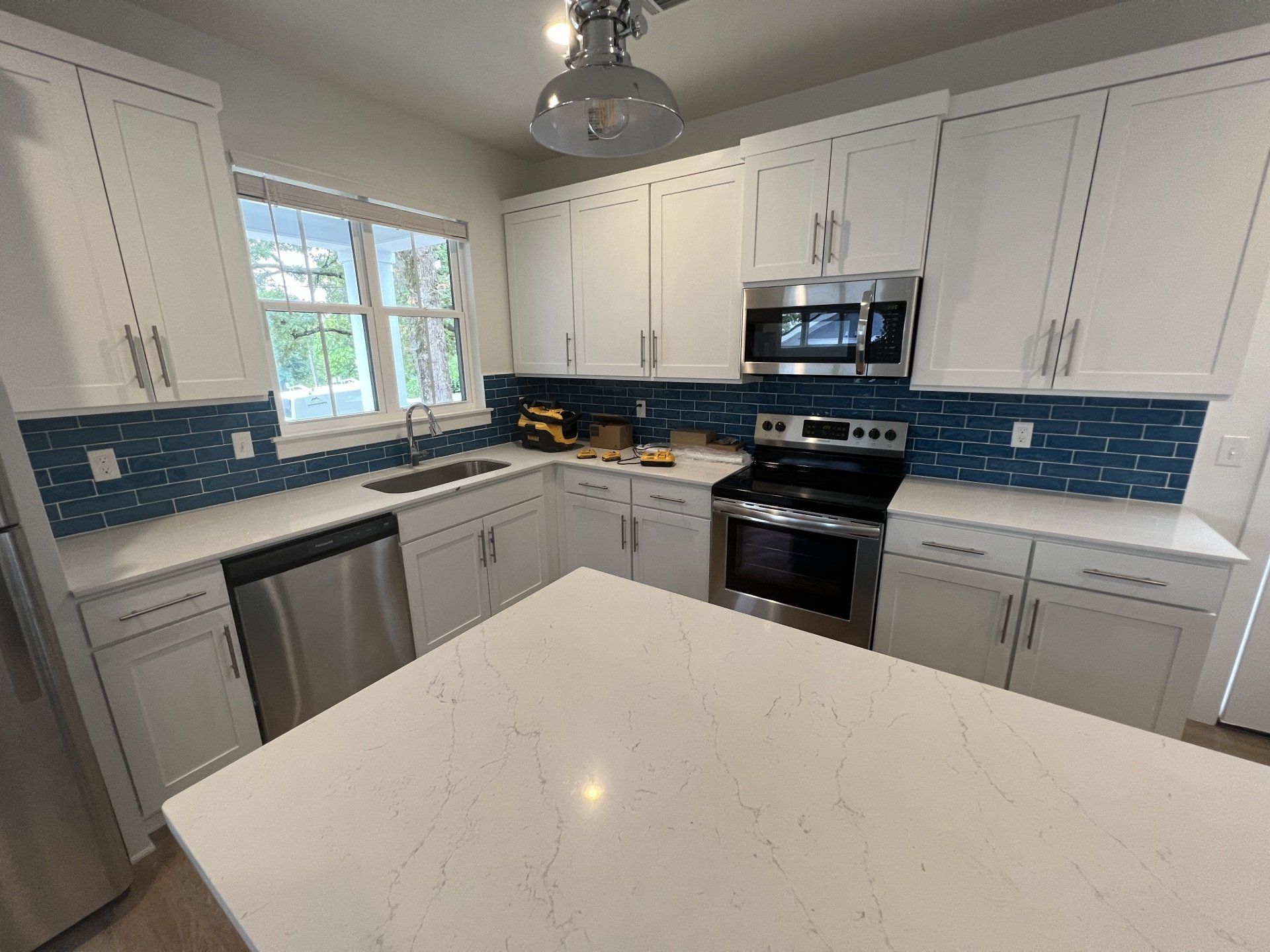 White kitchen with blue tile backsplash, stainless steel appliances, and large island.