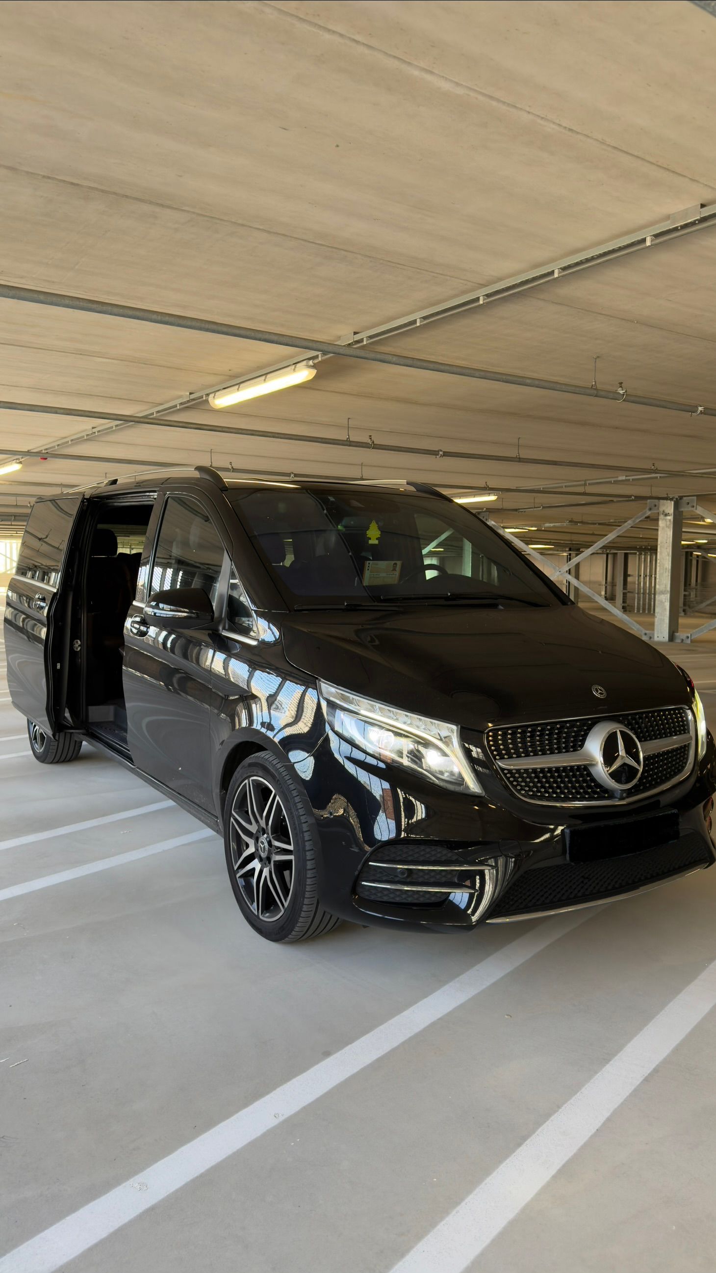 A black Mercedes-Benz van with its sliding door open, parked in a covered concrete parking garage.