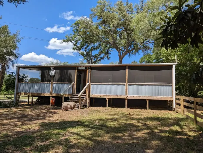 Mobile home with screened porch, wooden deck, corrugated metal siding, and trees. Sunny day.