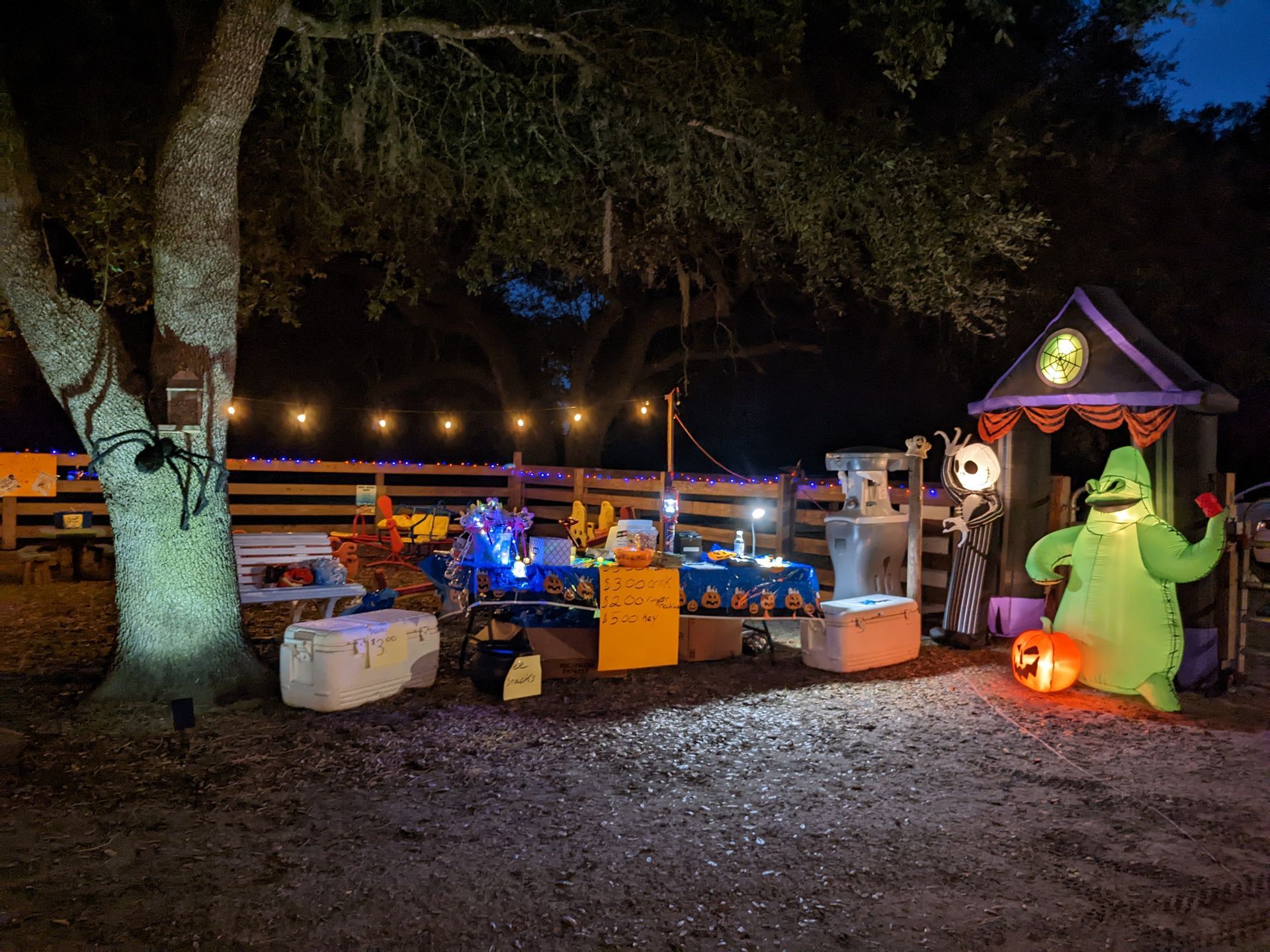 Halloween scene with lit decorations, including a house and Oogie Boogie inflatable figure, outdoors at night.