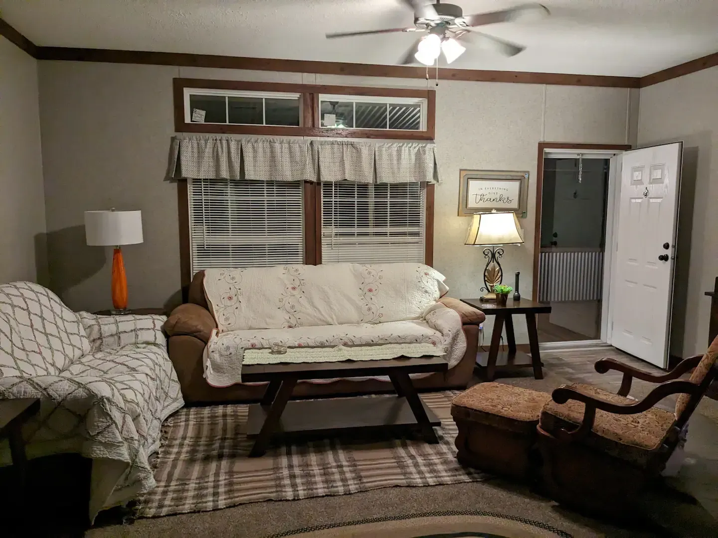 Cozy living room with brown sofa, rug, and armchair; door open to the outdoors.
