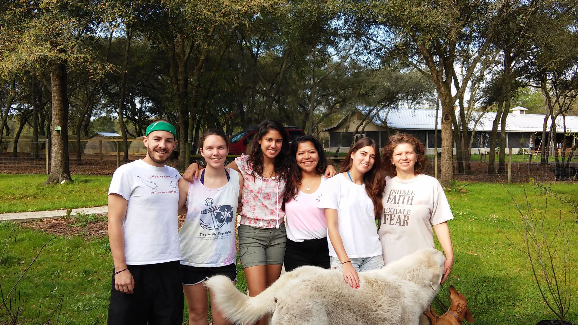 Group of people standing with a large white dog outside a house with trees.