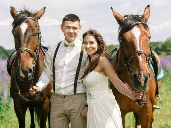 Wedding couple with two brown horses in a field, smiling, formal attire.