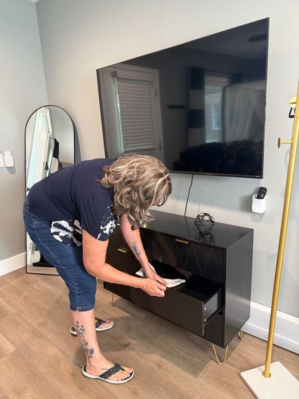 A person in a dark shirt and blue jeans bends over to open a drawer of a black media console under a wall-mounted TV.