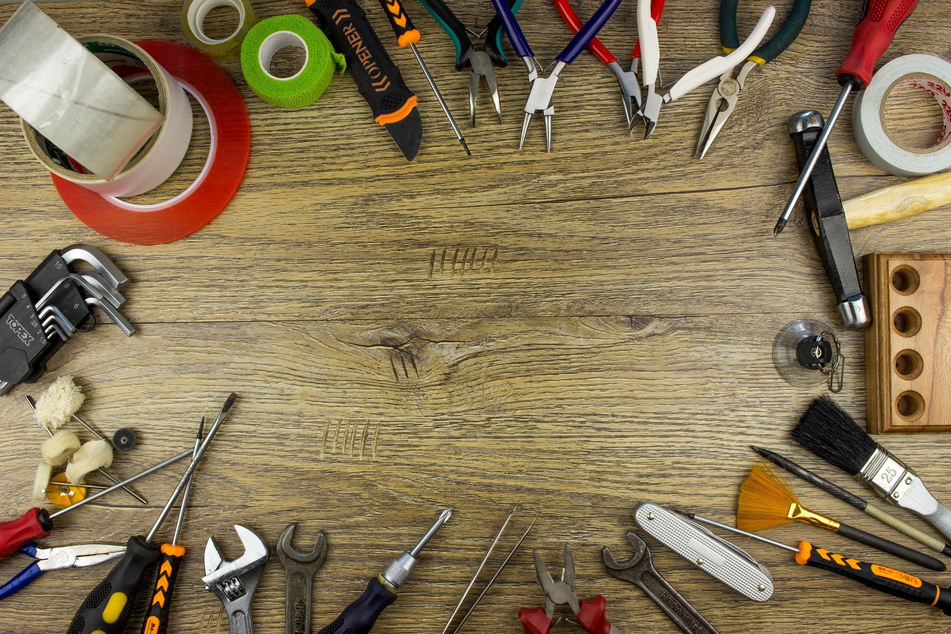 A top-down view of various household tools arranged in a border on a wooden surface, leaving space in the center.
