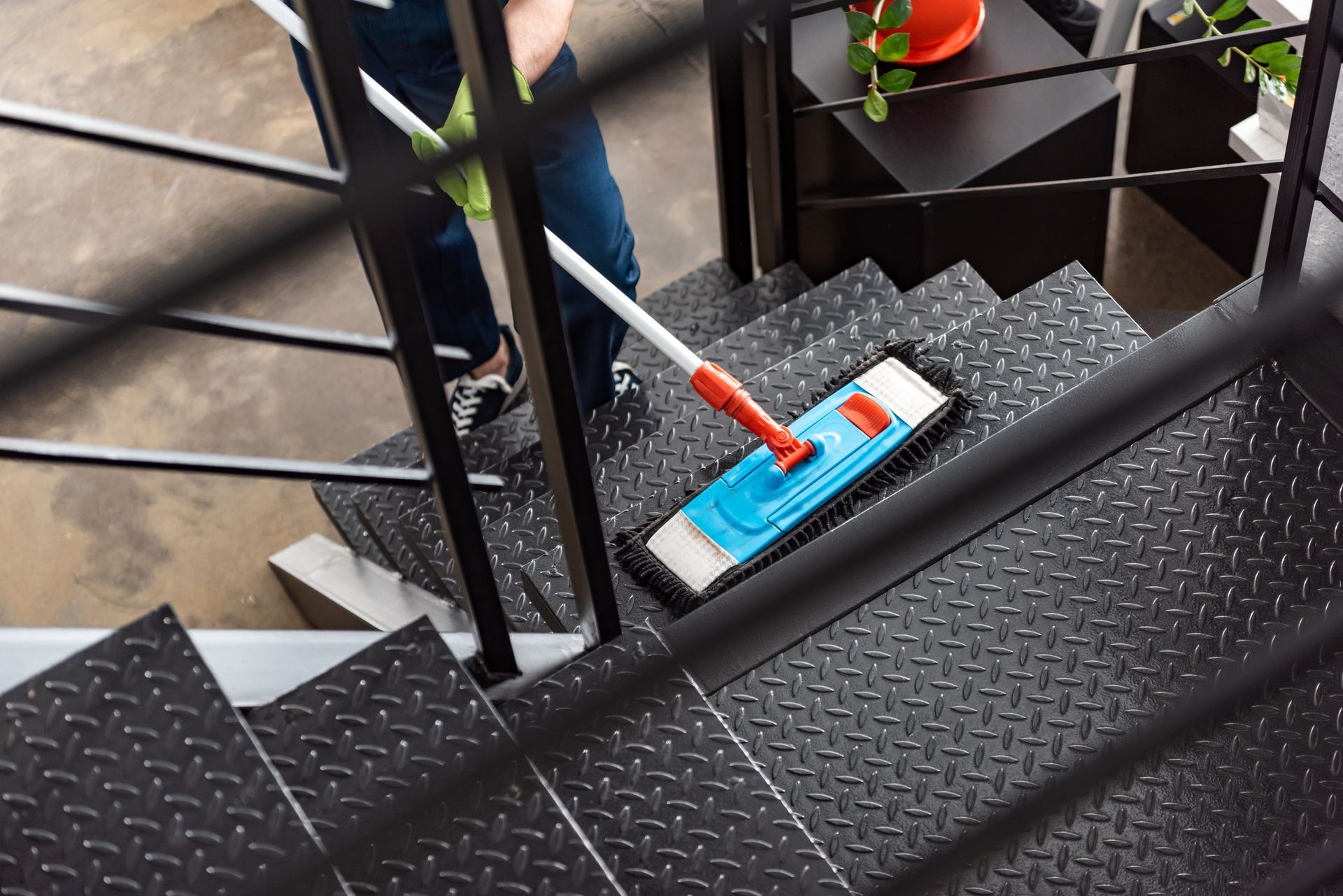 A person mopping a set of industrial, black metal stairs with a blue and white flat mop.