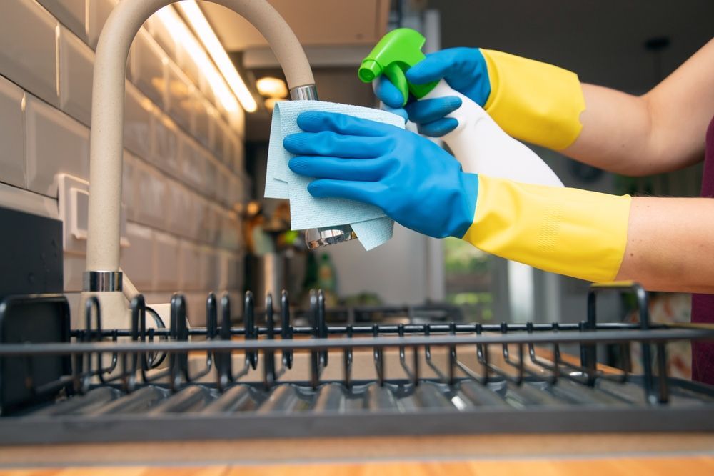 A person in gloves and shoe covers mops a wet tile floor in a hallway next to a yellow