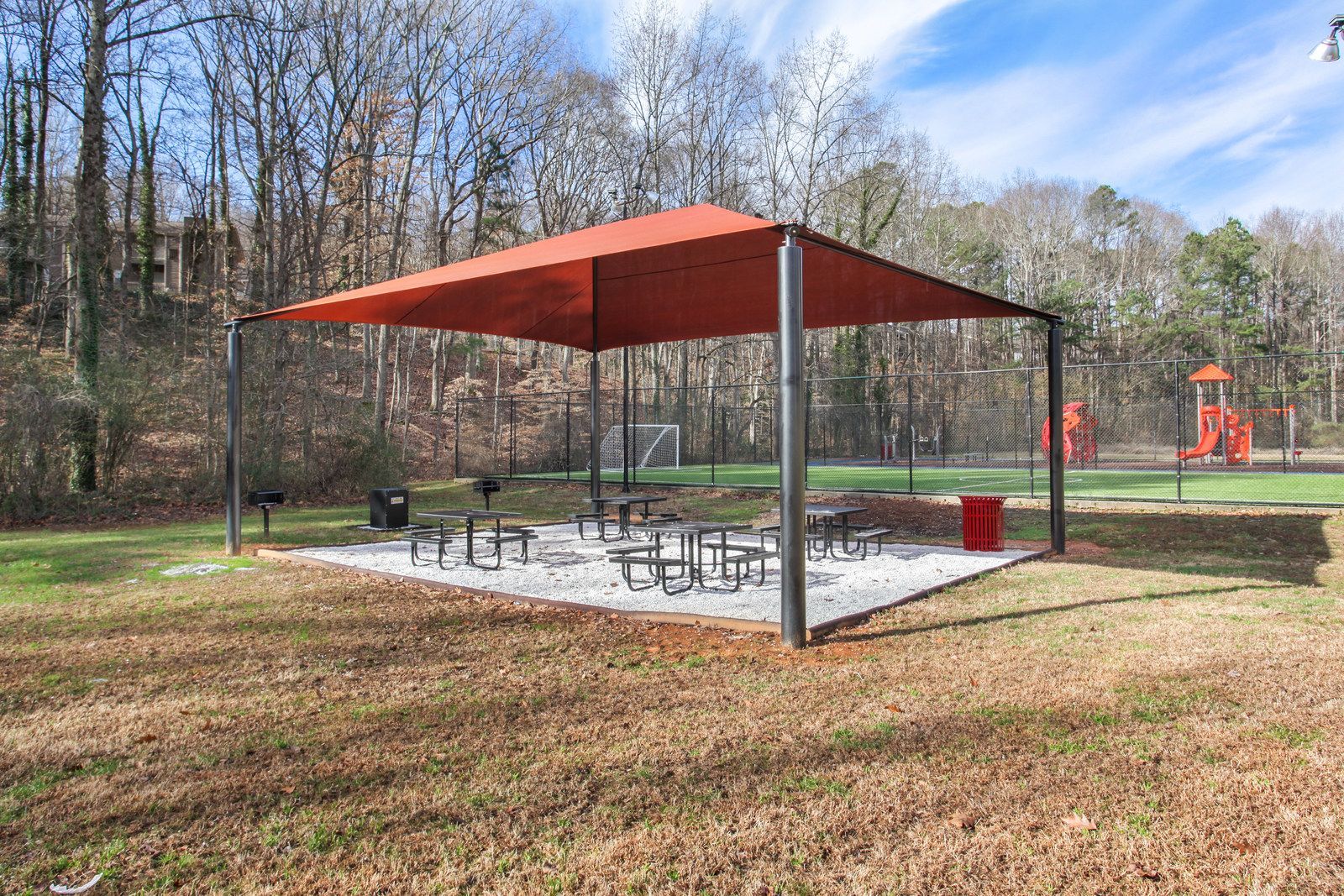 Park pavilion with red roof and picnic tables in a grassy wooded area