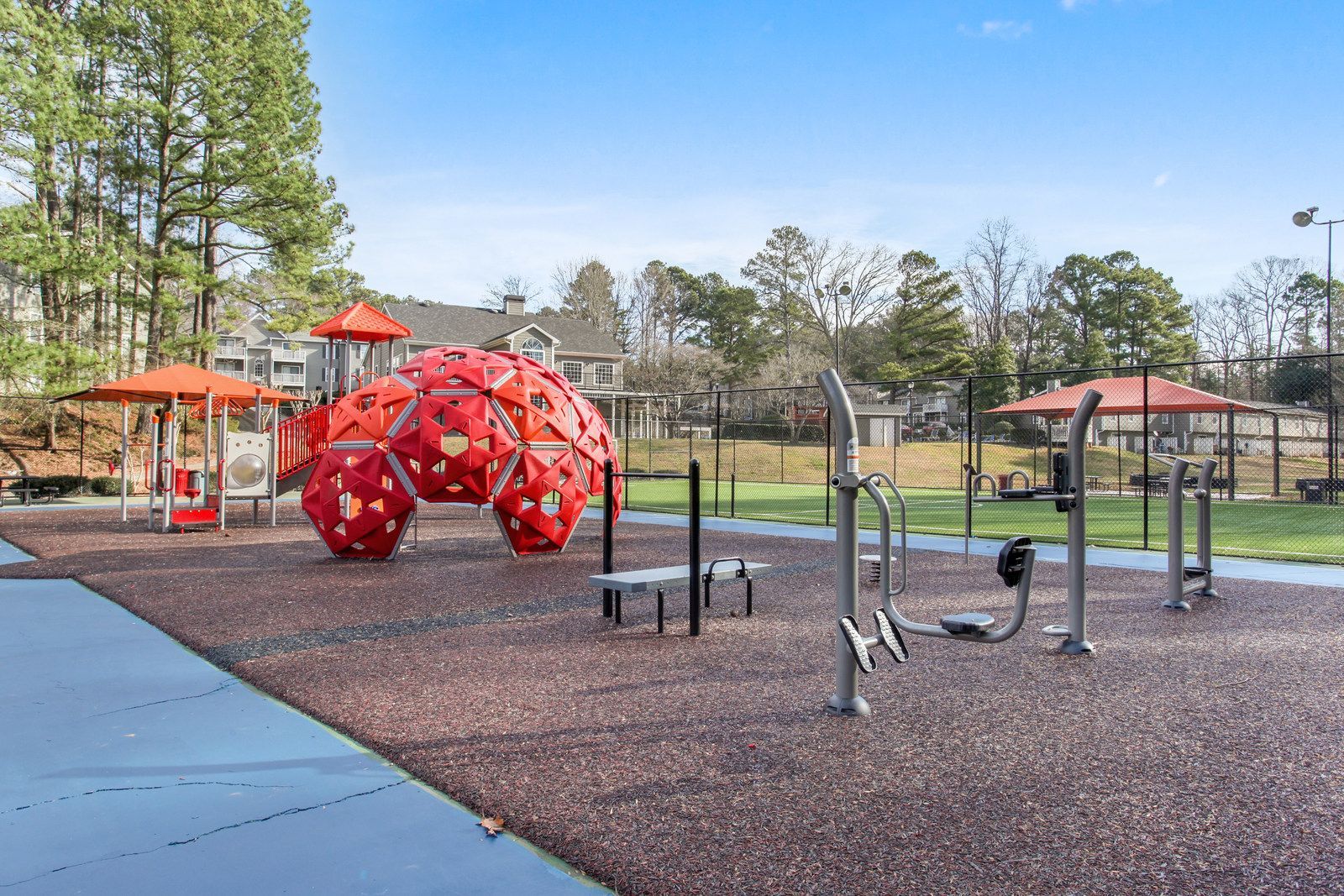 Outdoor playground with red climbing dome, exercise bars, and orange shade structures on rubber surfacing
