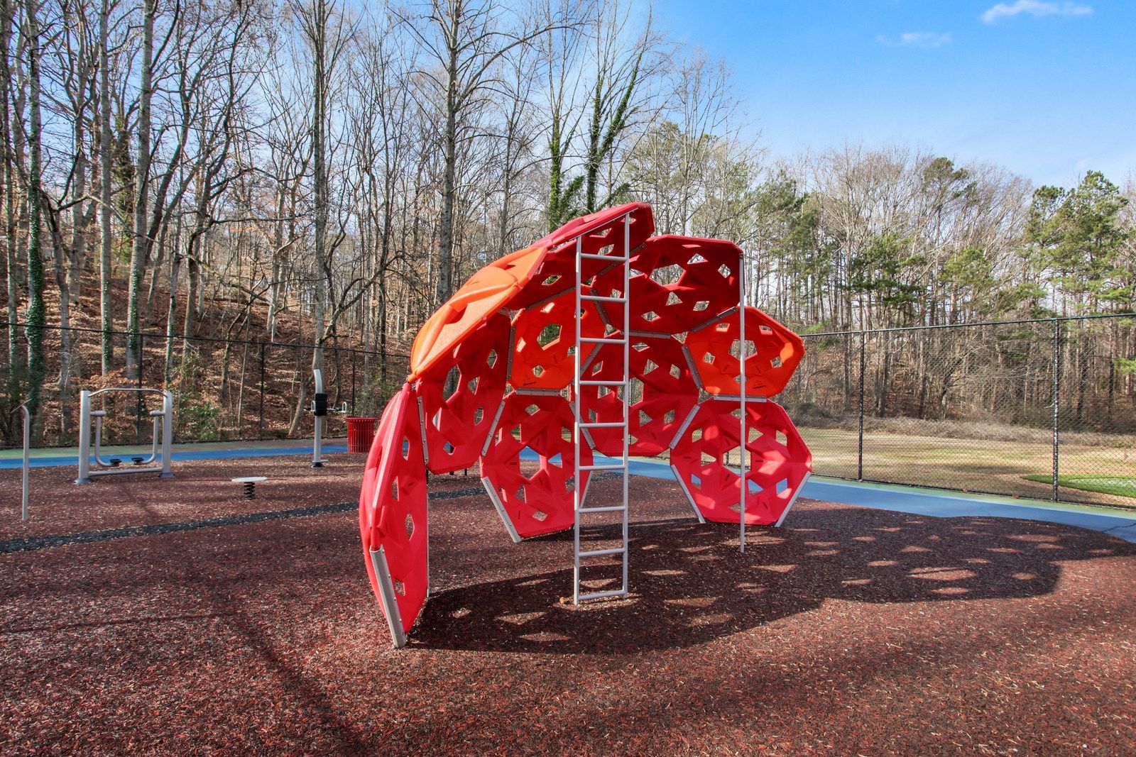 Red and orange climbing sculpture in a playground with a rope net and trees in the background