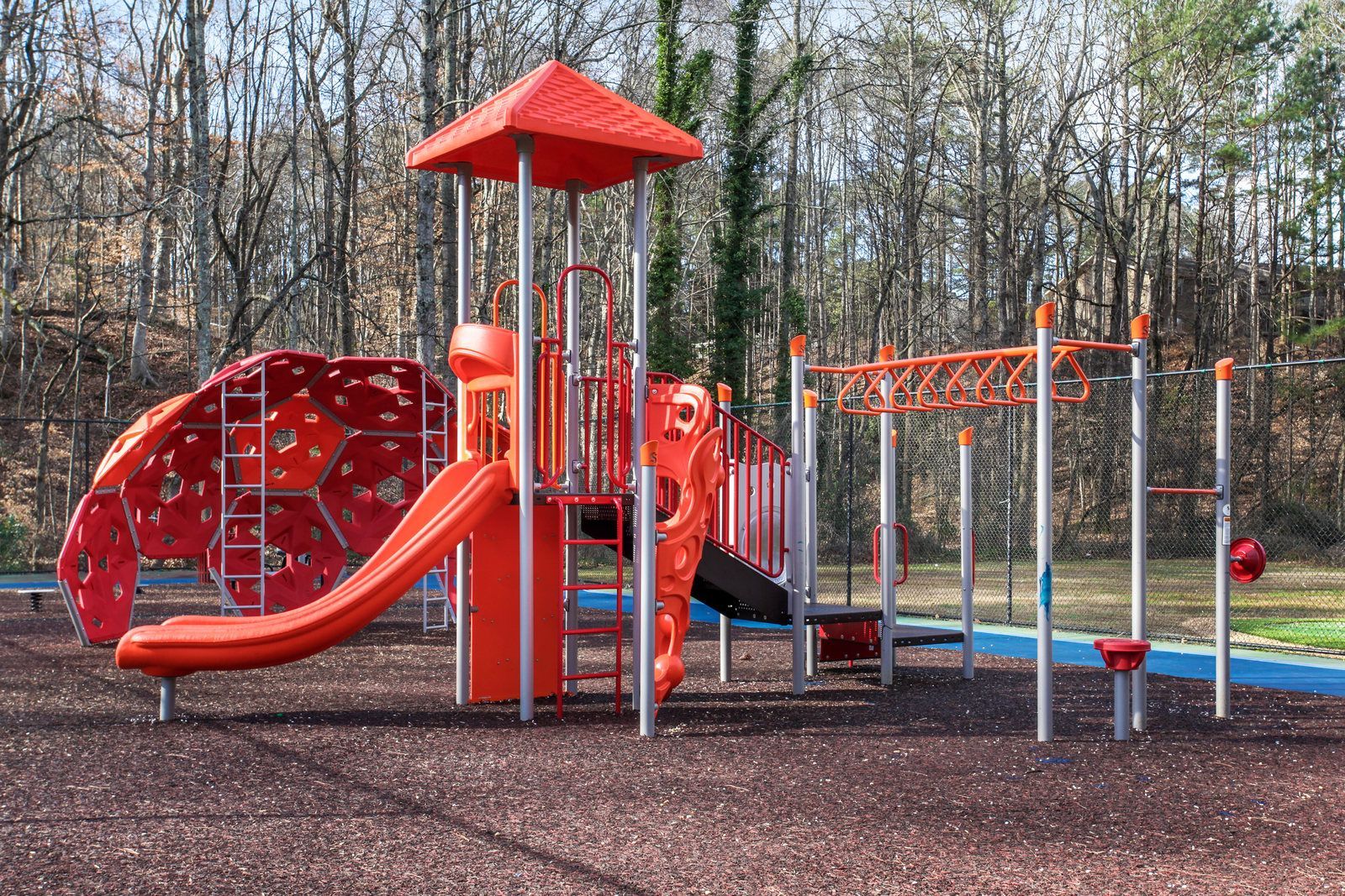 Colorful playground with red slide, climbing structure, and monkey bars in a wooded park
