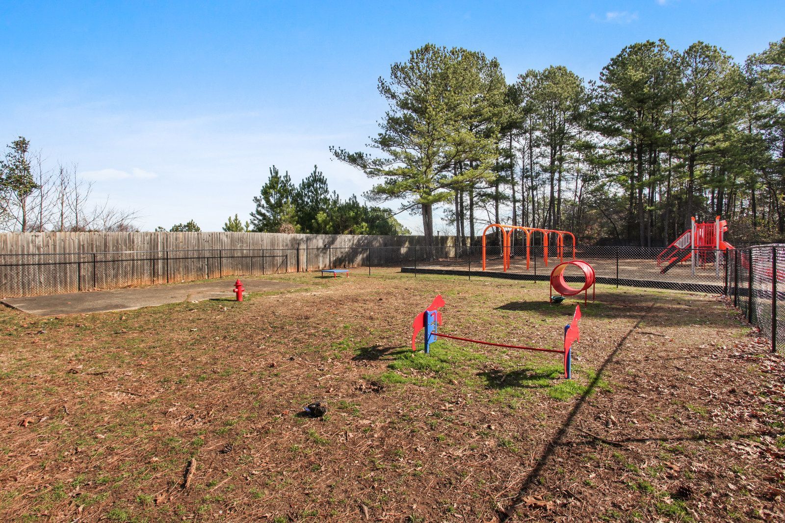 Empty playground with red equipment, leaf-covered ground, and trees under a clear sky