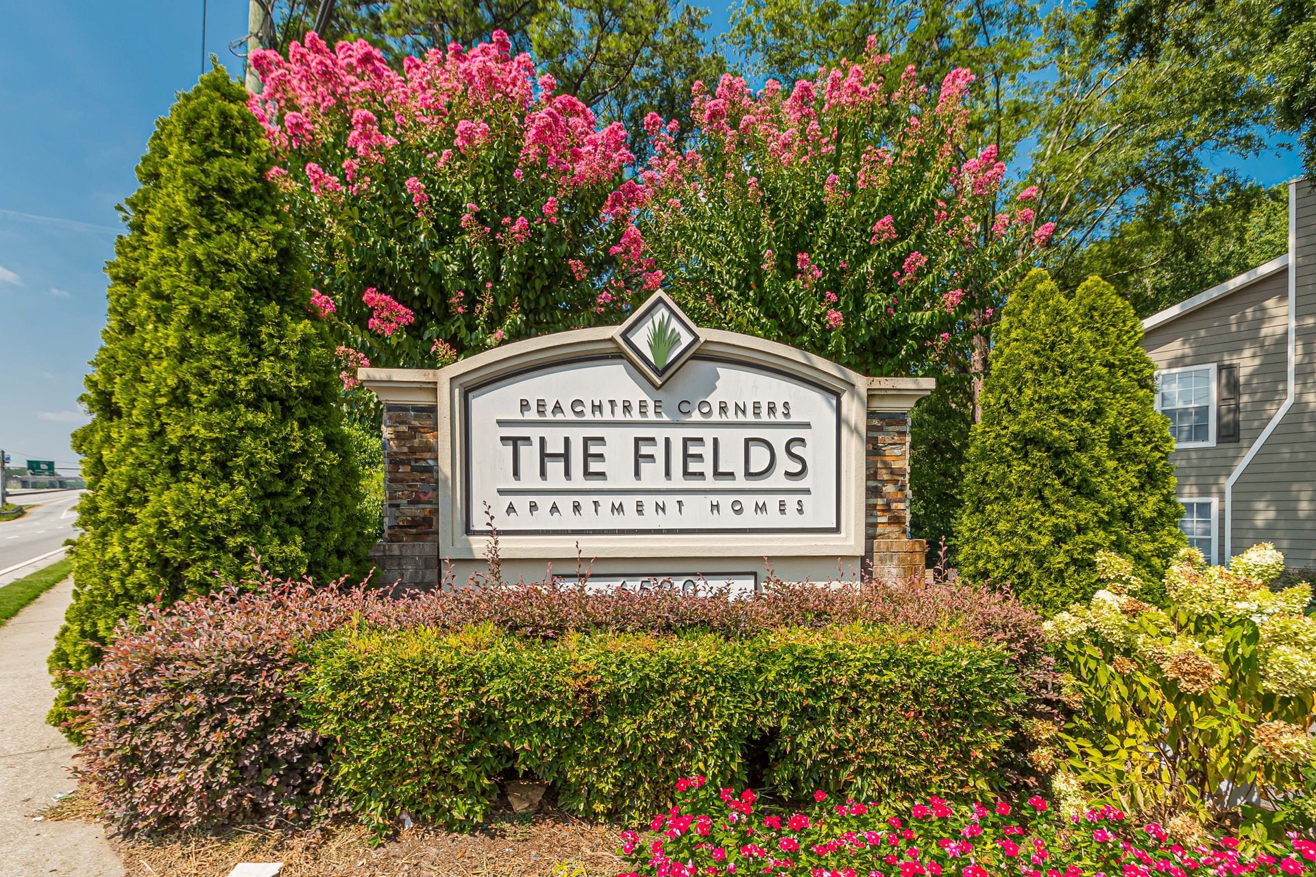 Apartment homes sign reading “The Fields” amid pink flowers and greenery outdoors