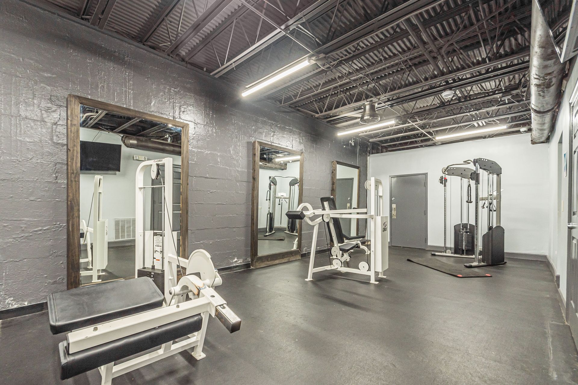 Empty gym interior with weight machines, mirrors, and overhead industrial lighting