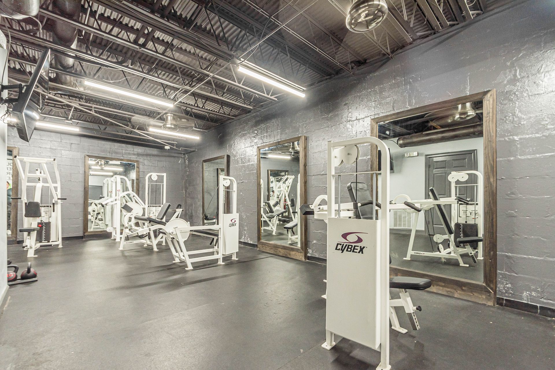 Modern gym interior with weight machines, mirrors, and industrial ceiling lighting