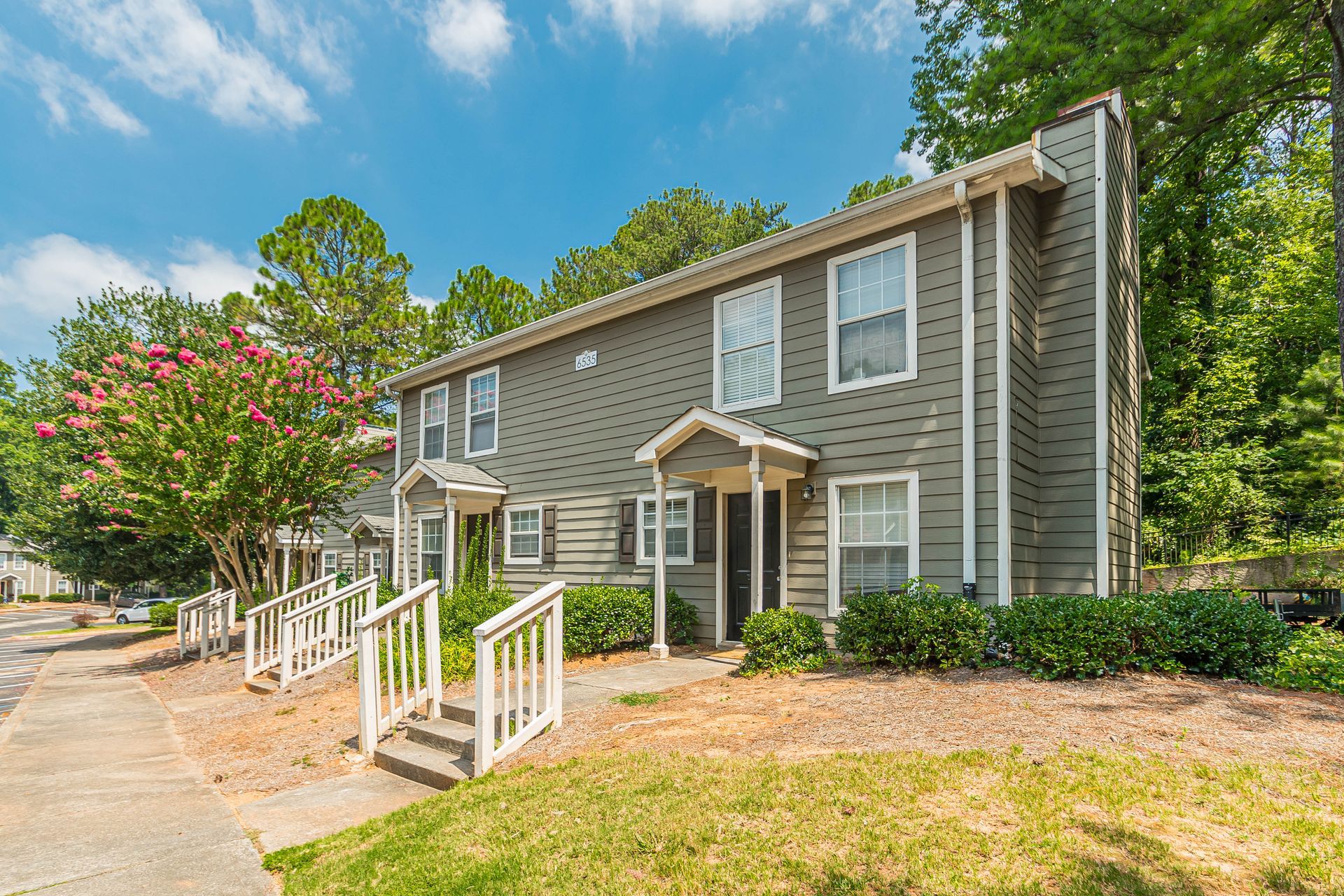 Apartment building exterior with white railings, gray siding, and trees under a blue sky