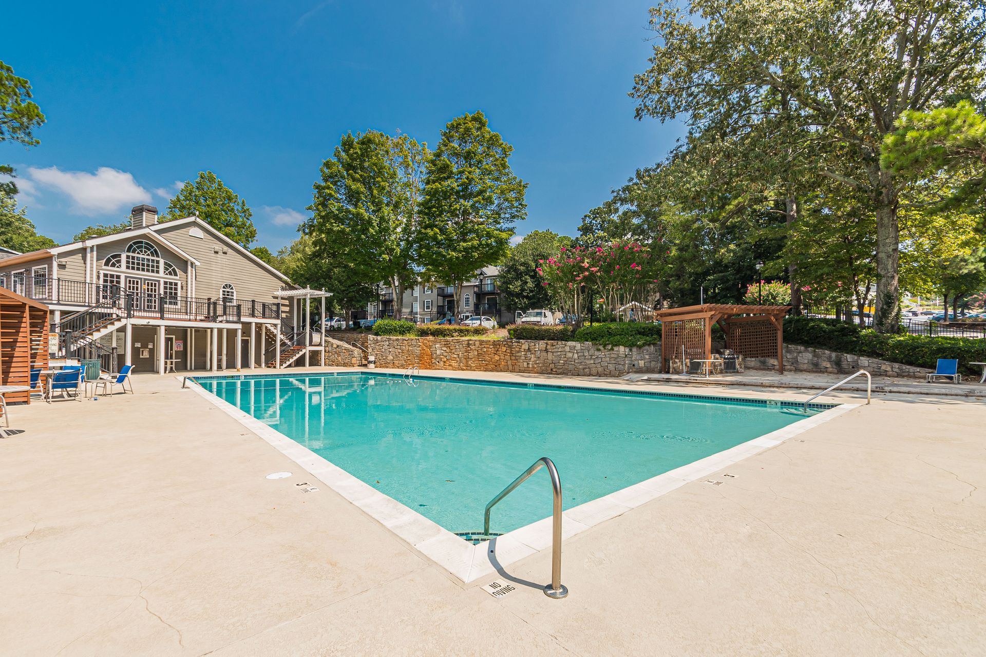 Outdoor apartment pool with turquoise water, lounge chairs, and trees on a sunny day