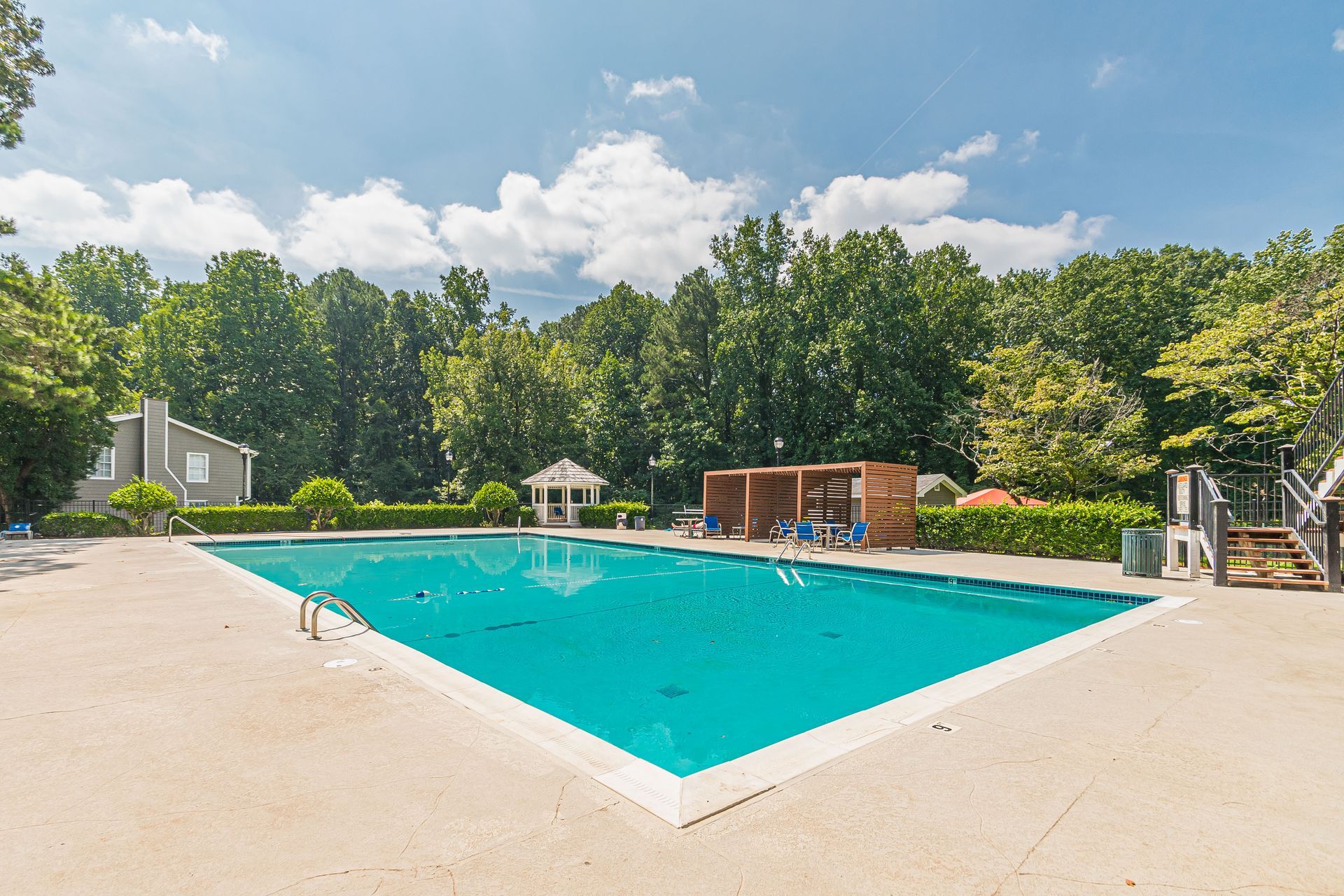 Outdoor swimming pool with turquoise water, lounge chairs, and trees under a bright sky