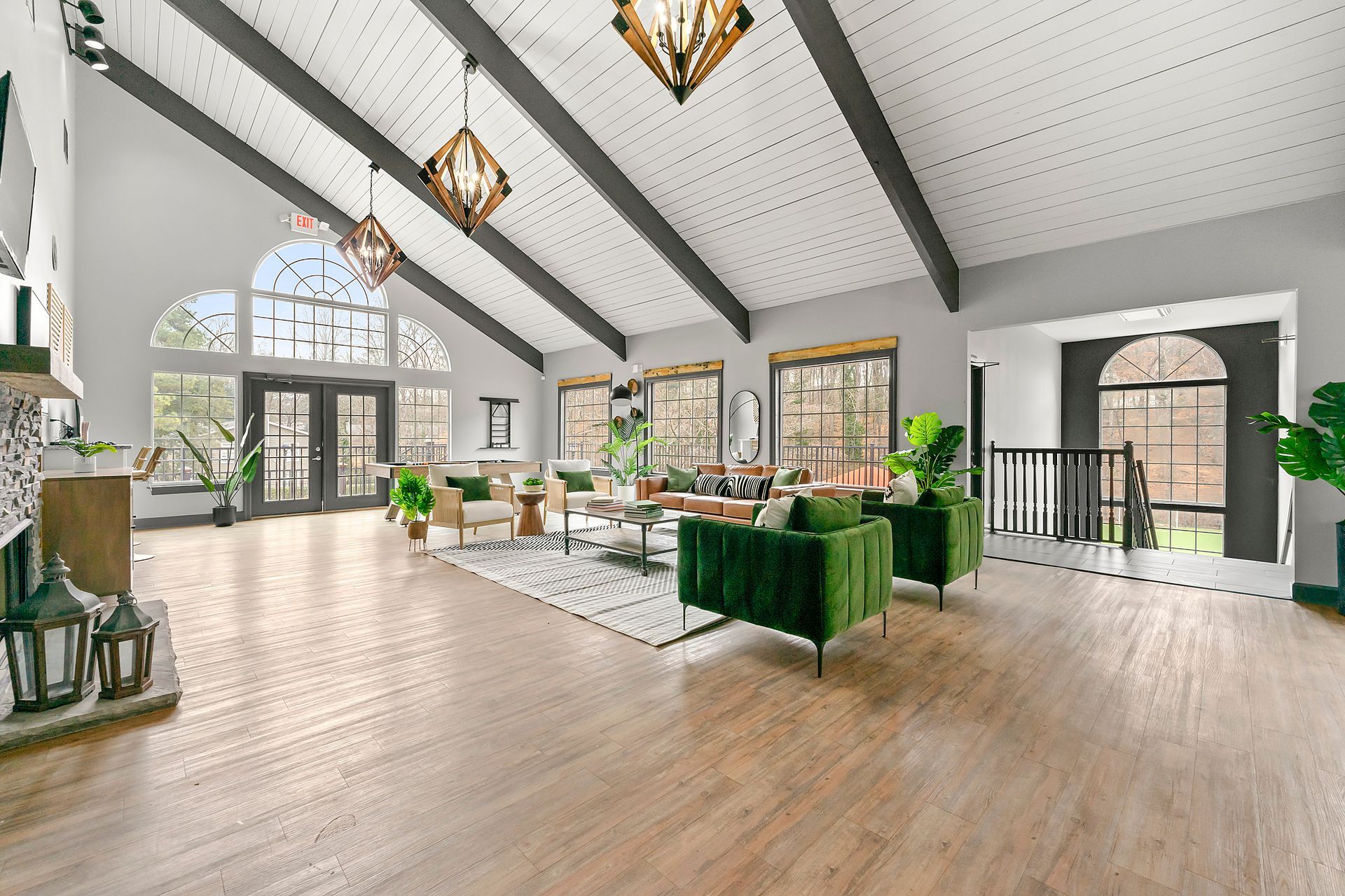 Bright modern living room with high vaulted ceiling, green sofas, large windows, and wood floors