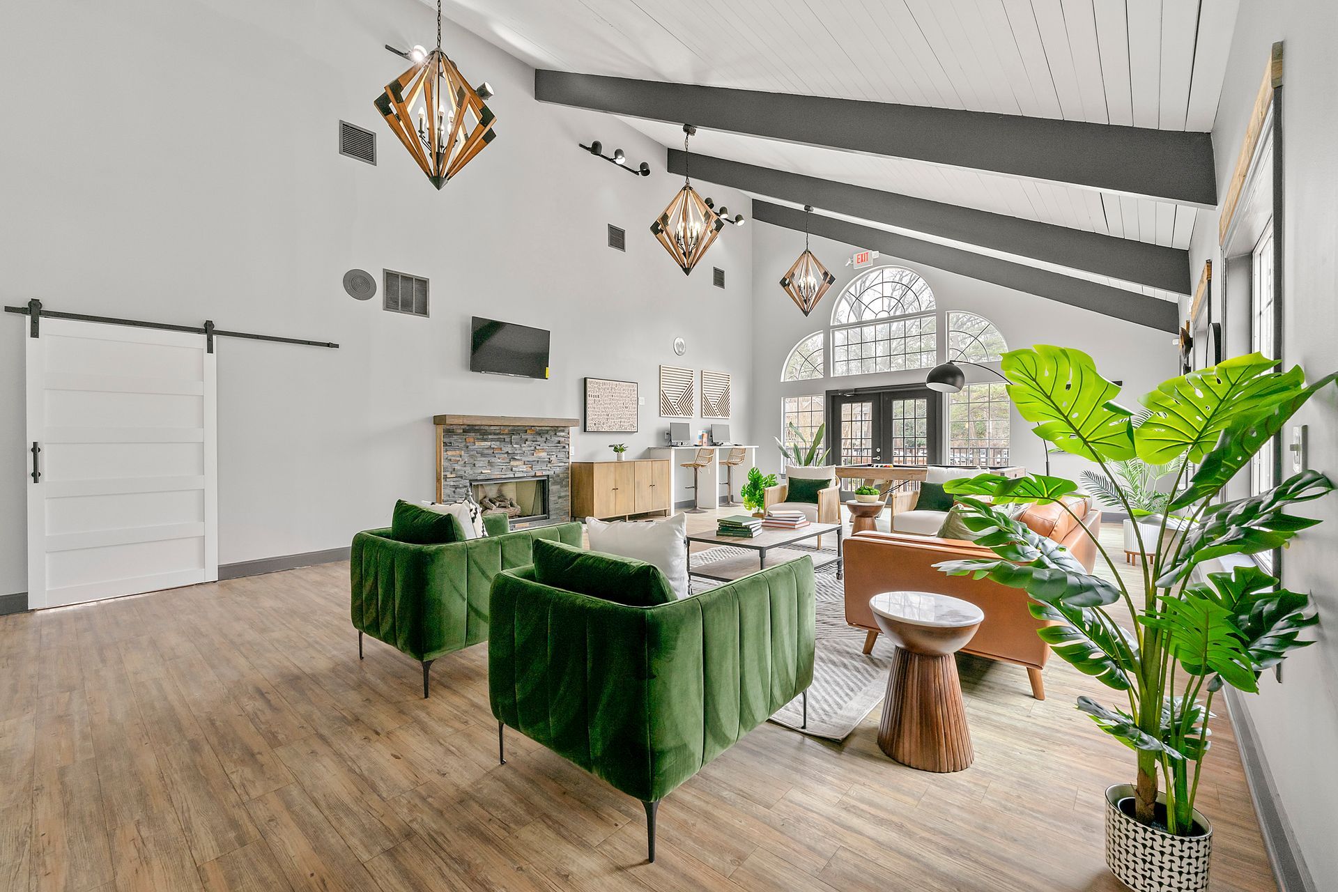 Bright modern living room with green velvet chairs, wood floors, large windows, and potted plants