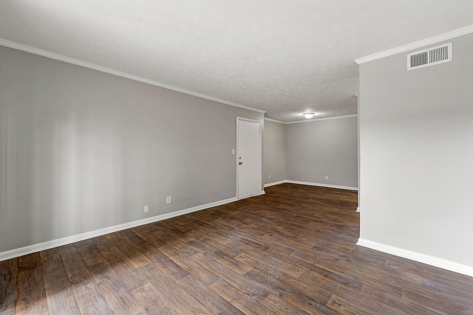 Empty living room with gray walls, wood floors, and a doorway to a bright adjoining space.
