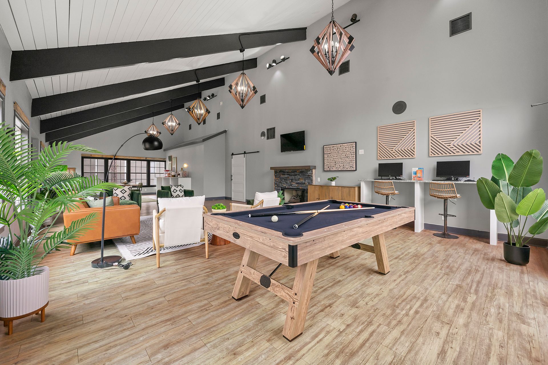 Bright game room with pool table, hanging lights, wood floors, and indoor plants.