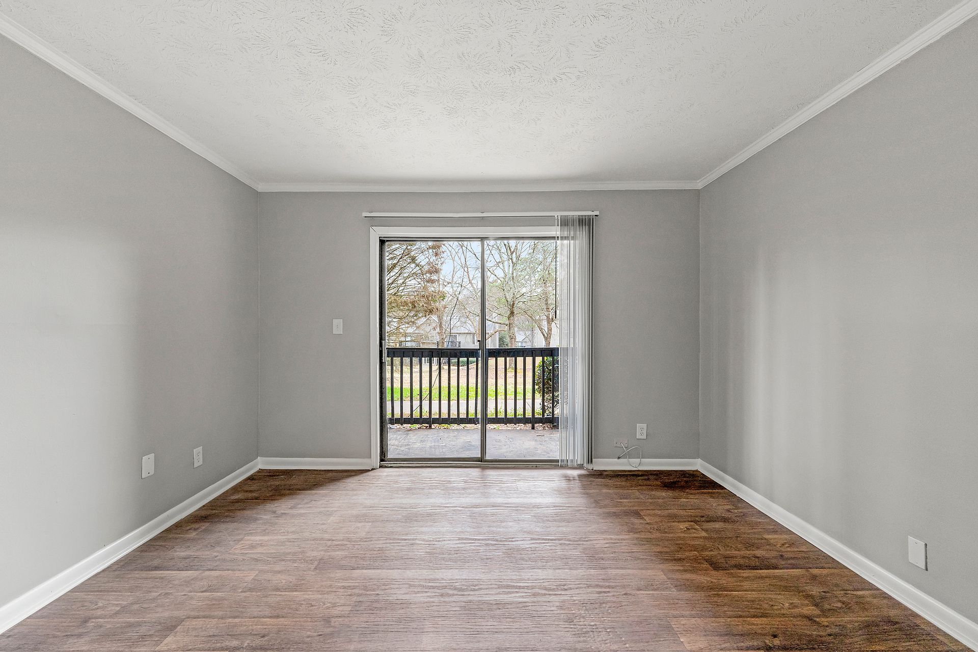 Empty gray living room with wood floors and sliding glass doors to a balcony
