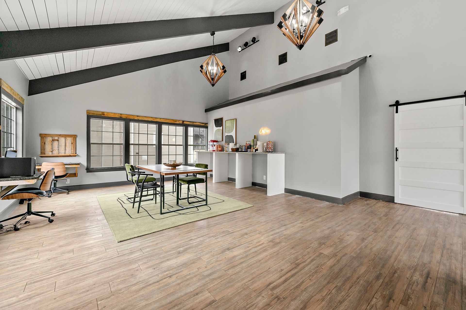 Bright, modern open room with wood floors, glass tables, stools, and a white counter beneath hanging lights