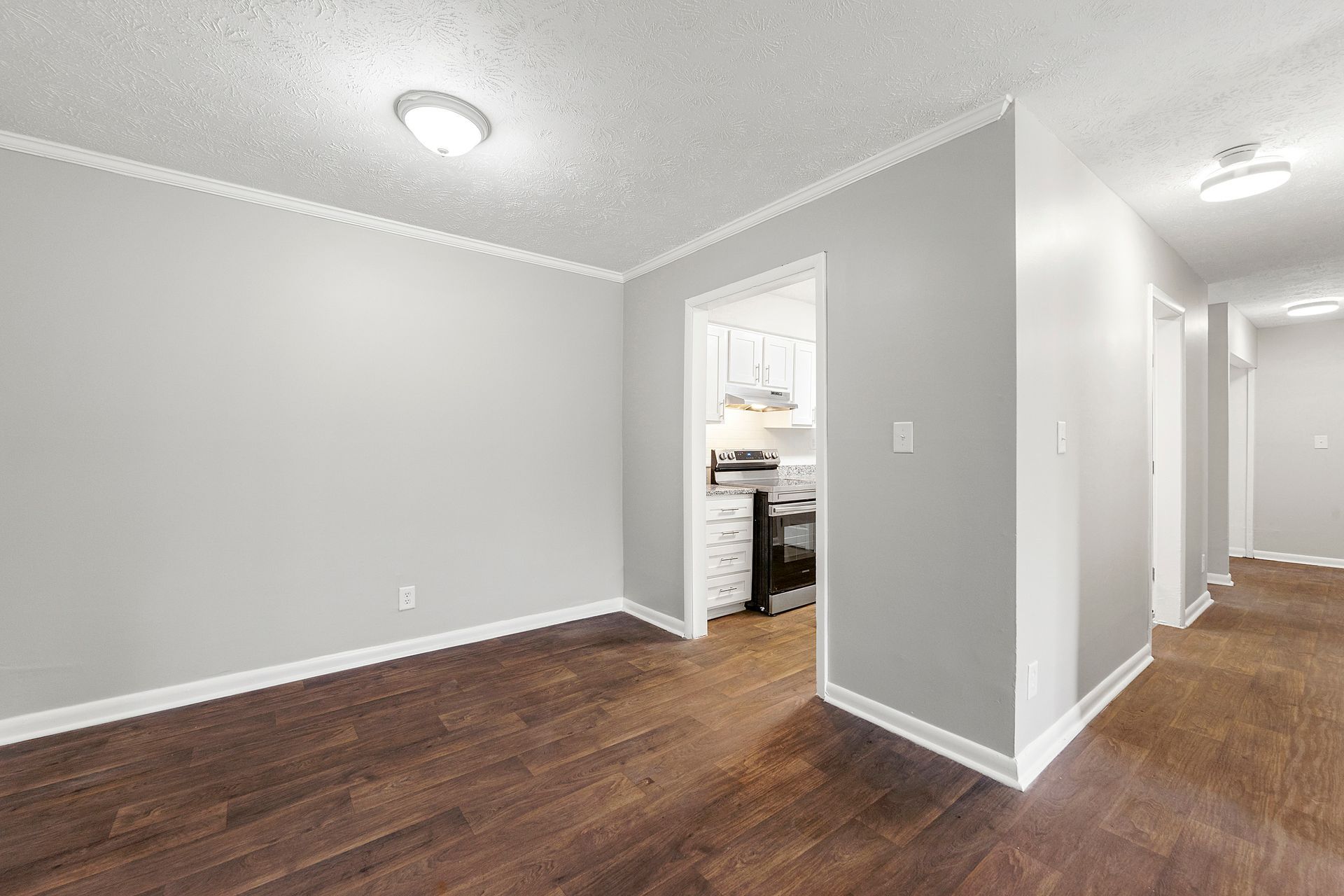 Empty gray living room with dark wood floors and a doorway to a bright adjacent room