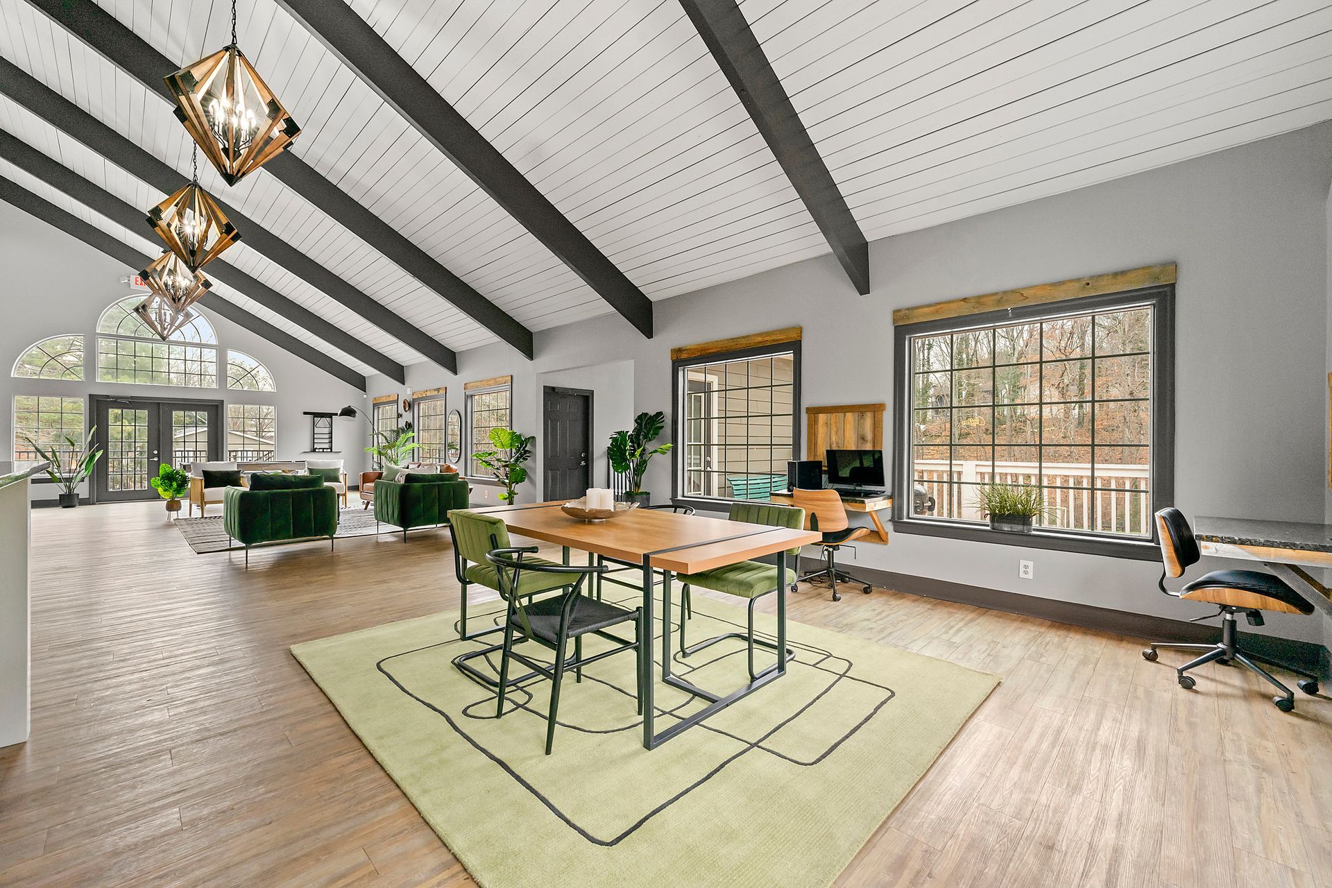 Bright open living room with vaulted ceiling, wood beams, large windows, and a central dining table on a rug