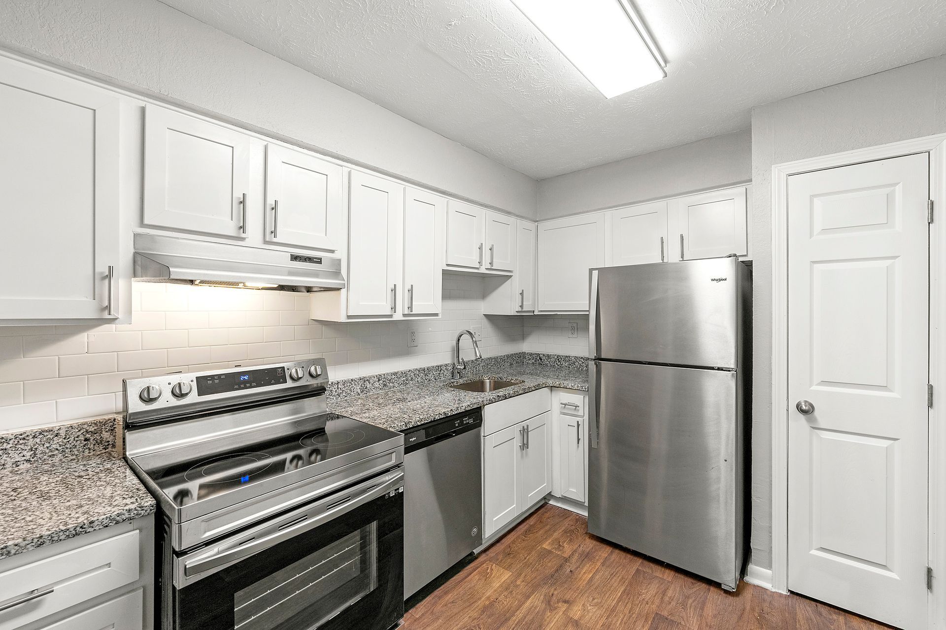 Bright kitchen with white cabinets, stainless steel appliances, granite counters, and wood flooring