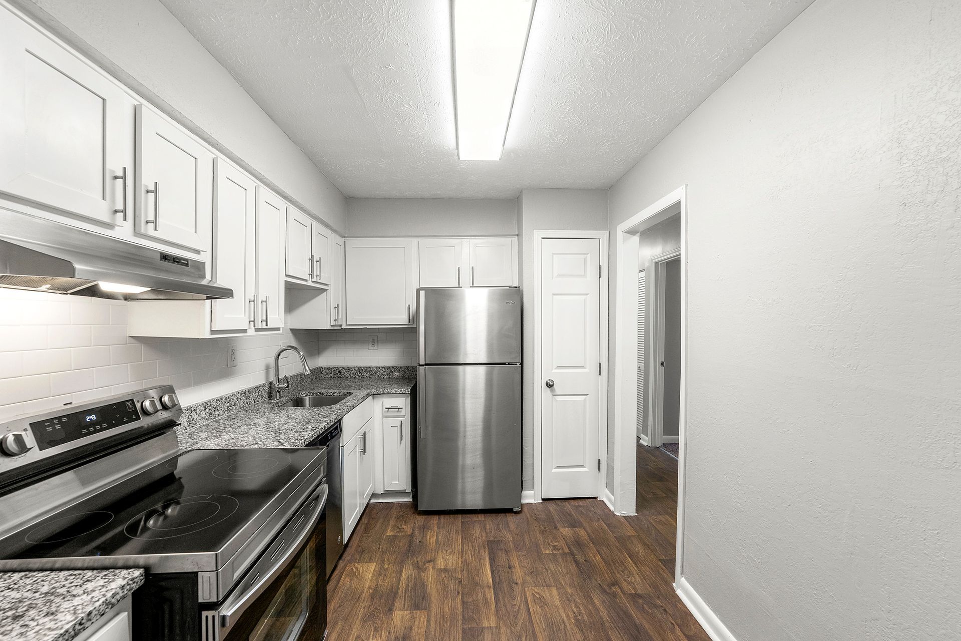Bright white galley kitchen with stainless steel appliances, granite counters, and wood flooring.