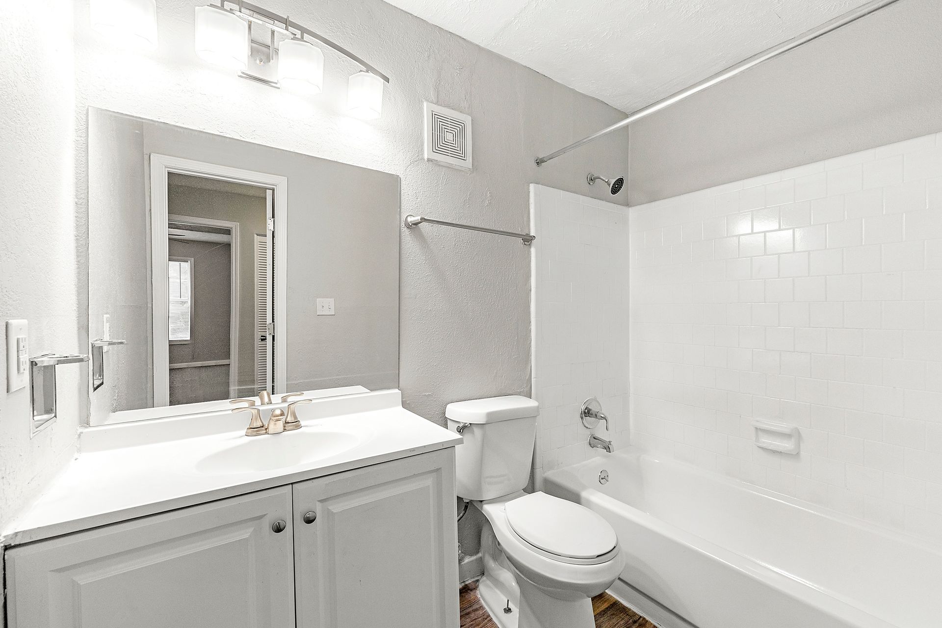 Bright white bathroom with sink, mirror, toilet, and bathtub.