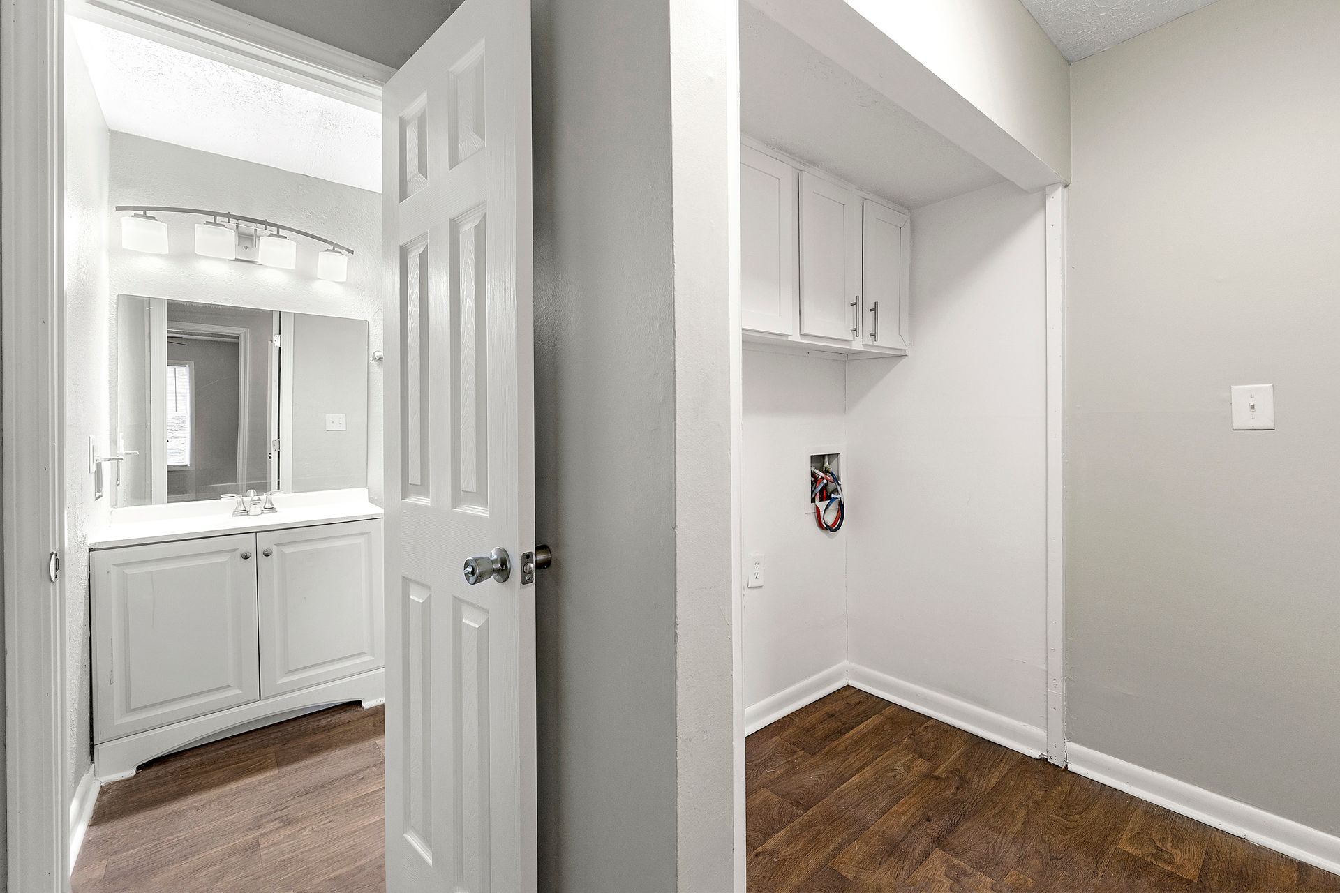 Hallway with bathroom vanity on left and small closet alcove on right, white walls and wood floor
