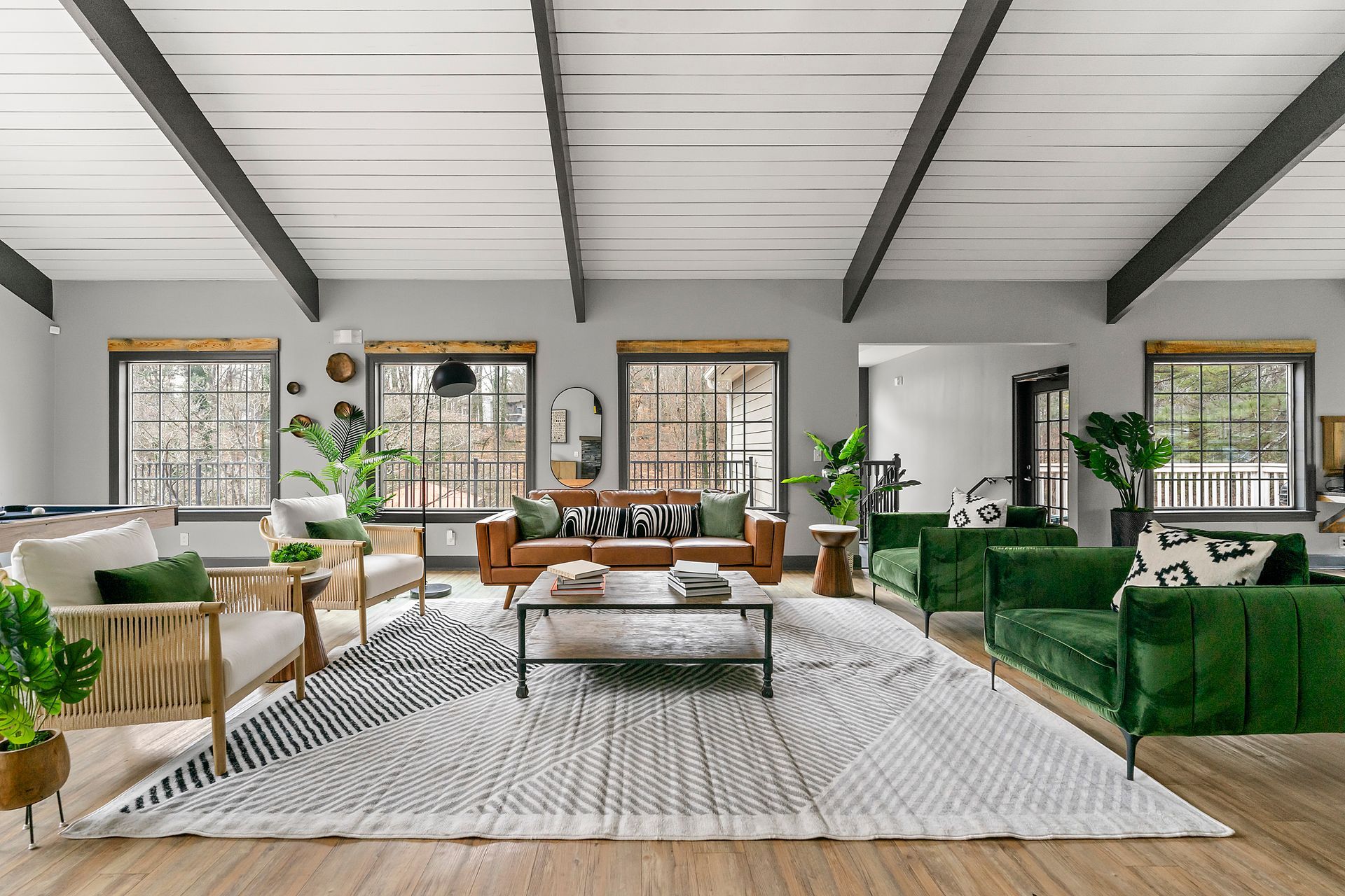 Bright living room with green sofas, woven chairs, large rug, and high vaulted ceiling with exposed beams