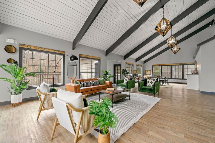 Bright open living room with white sofas, wood floors, high beam ceiling, and large windows