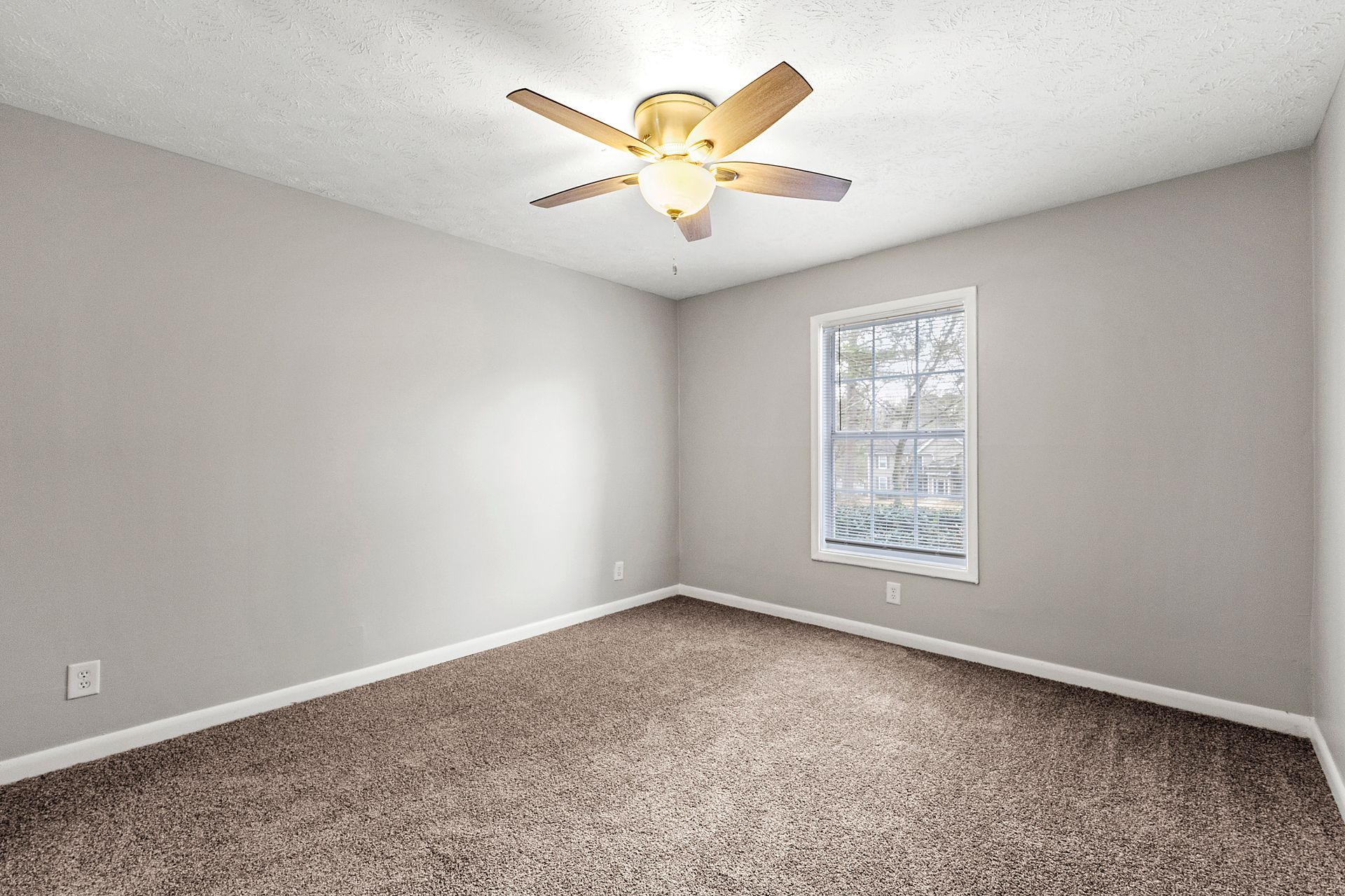 Empty gray bedroom with carpet, ceiling fan, and a window on the right wall