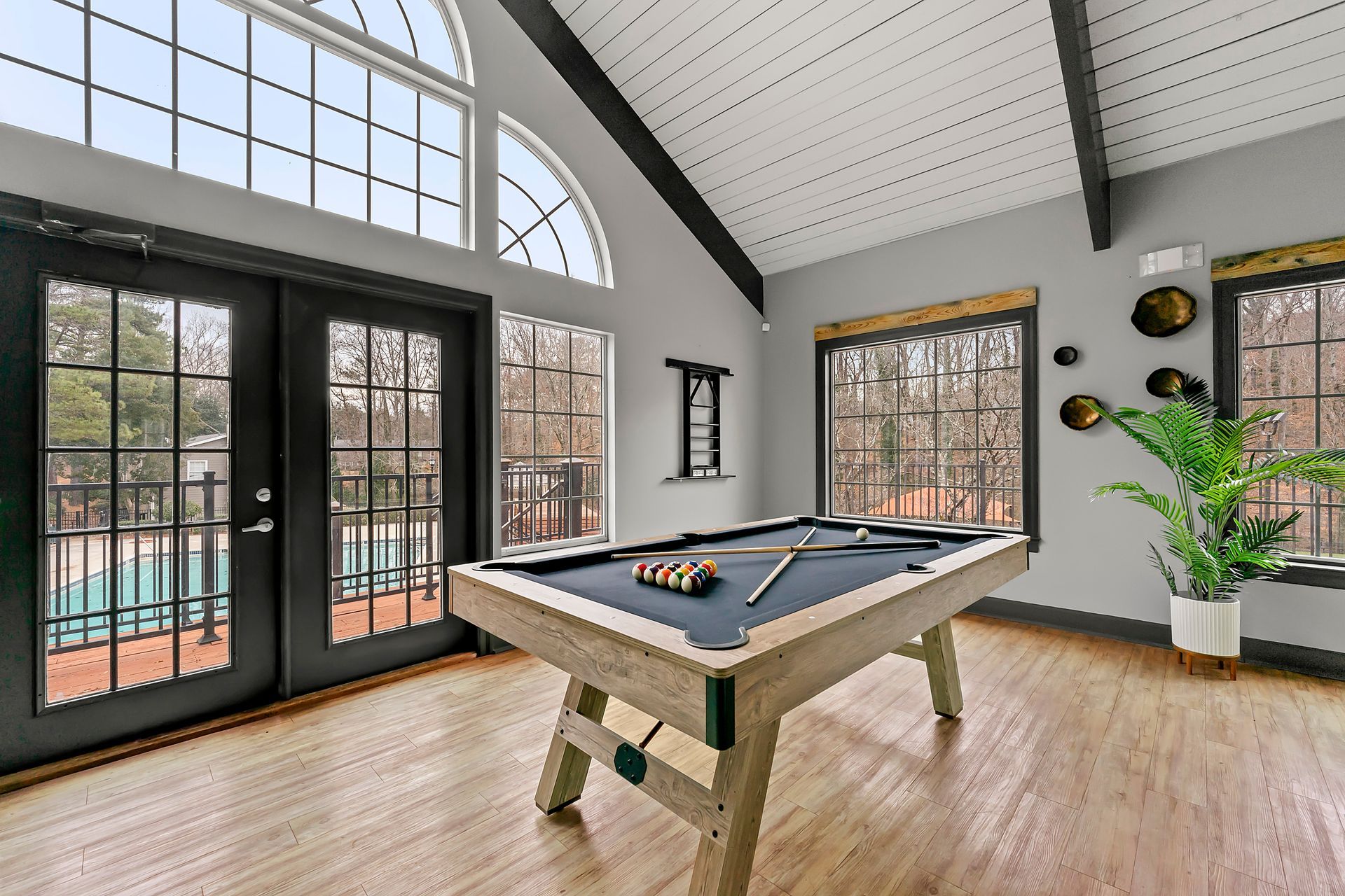 Spacious game room with a pool table, large arched windows, and light wood floors.